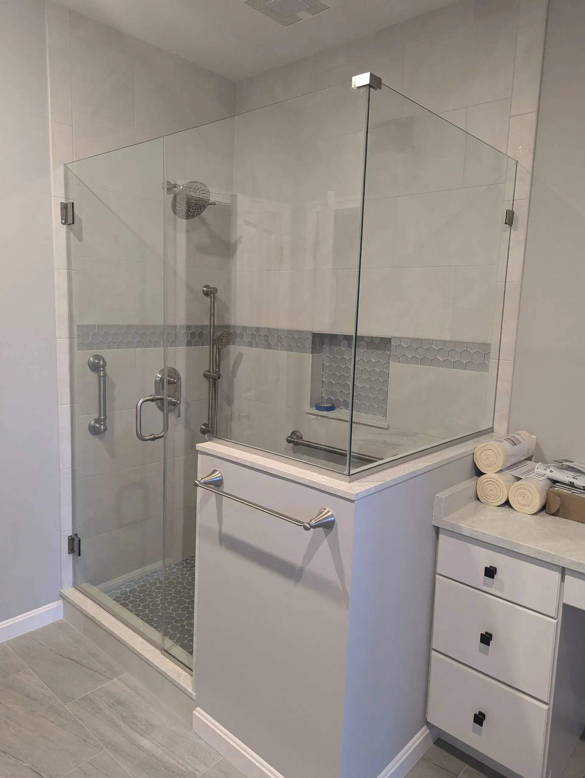 Modern tiled bathroom with a glass-enclosed shower, white vanity, and marble-top counter.