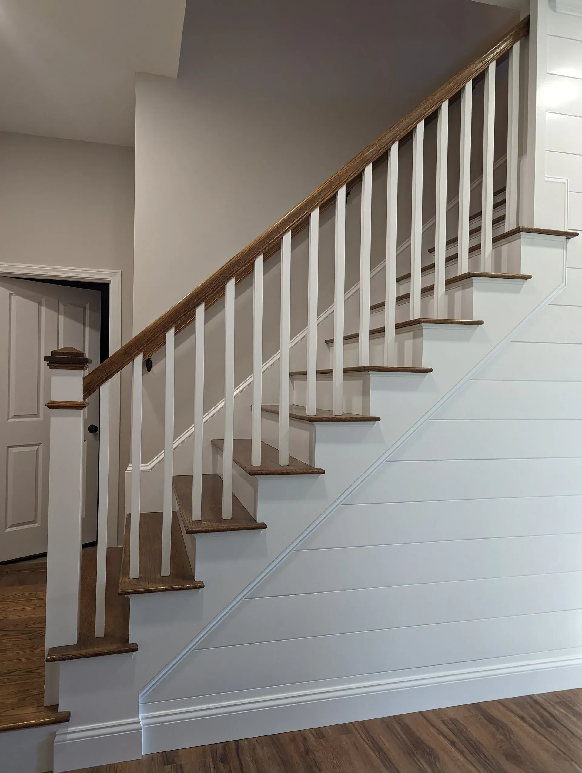 Indoor staircase with white balusters and wooden handrail beside a hallway and door