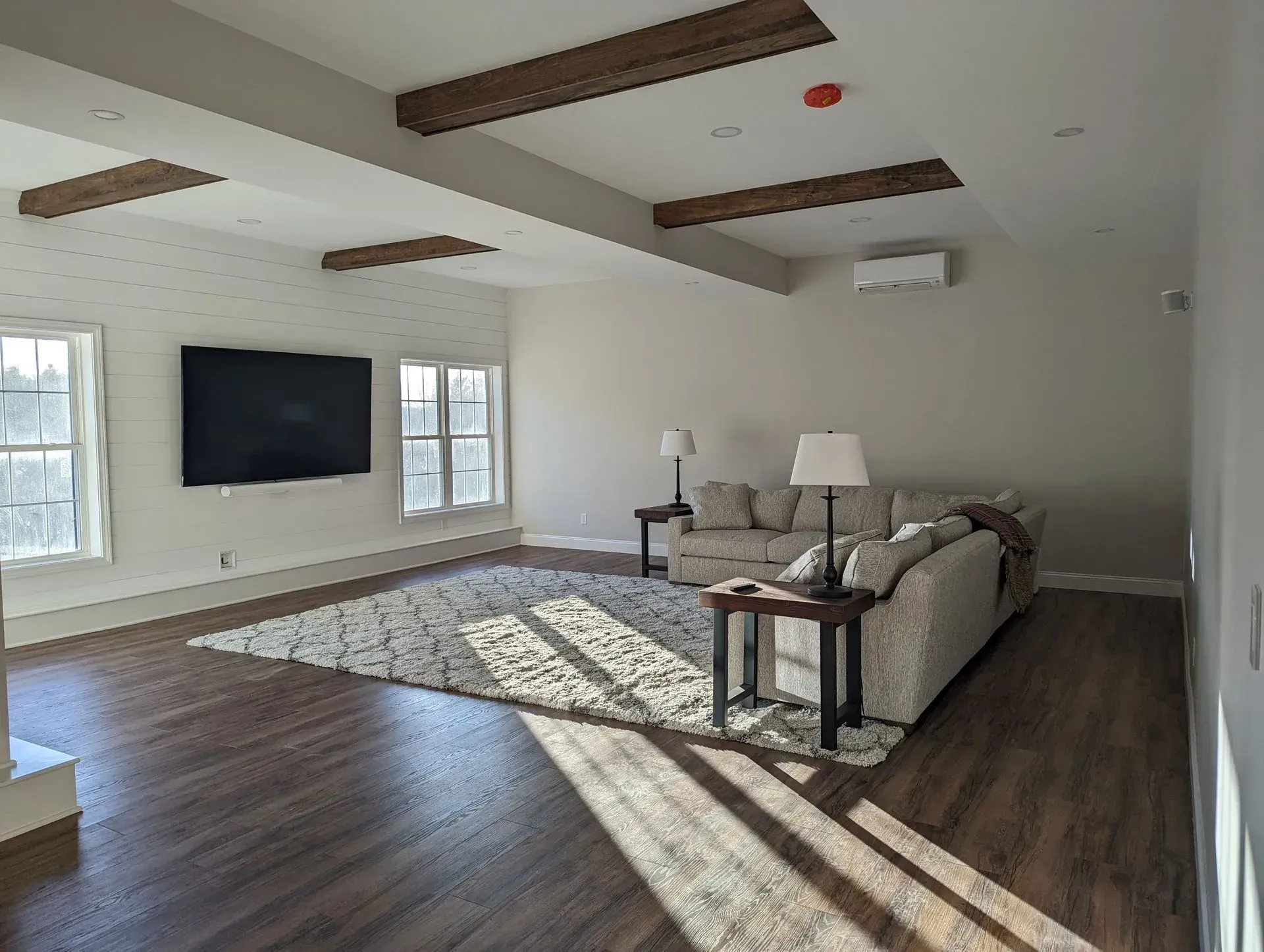 Bright living room with wall-mounted TV, sofa, rug, and sunlit windows