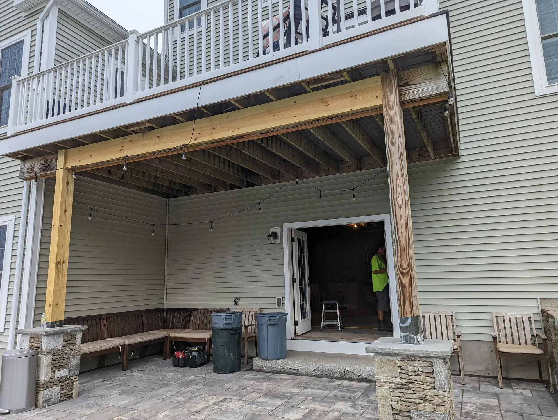Covered backyard deck under construction with exposed beams, open doorway, and tools below the balcony