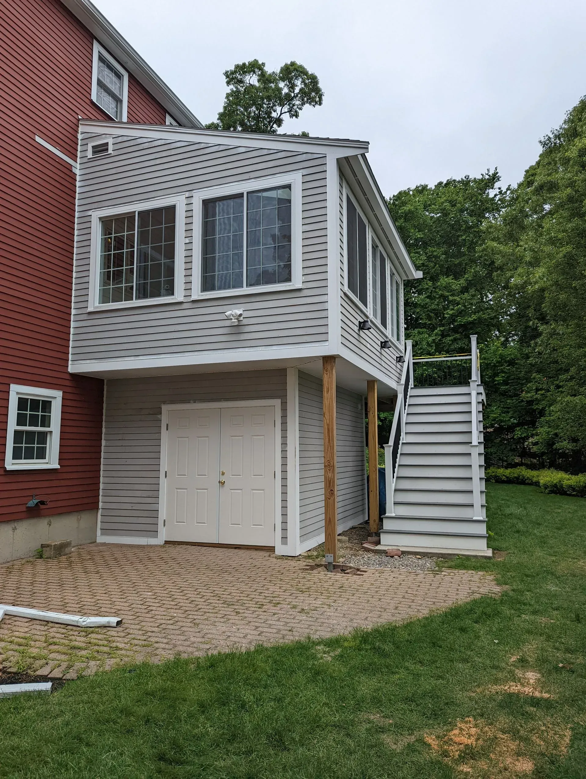 Small white screened porch extension on a red brick house, with stairs, doors, and a cobblestone patio below