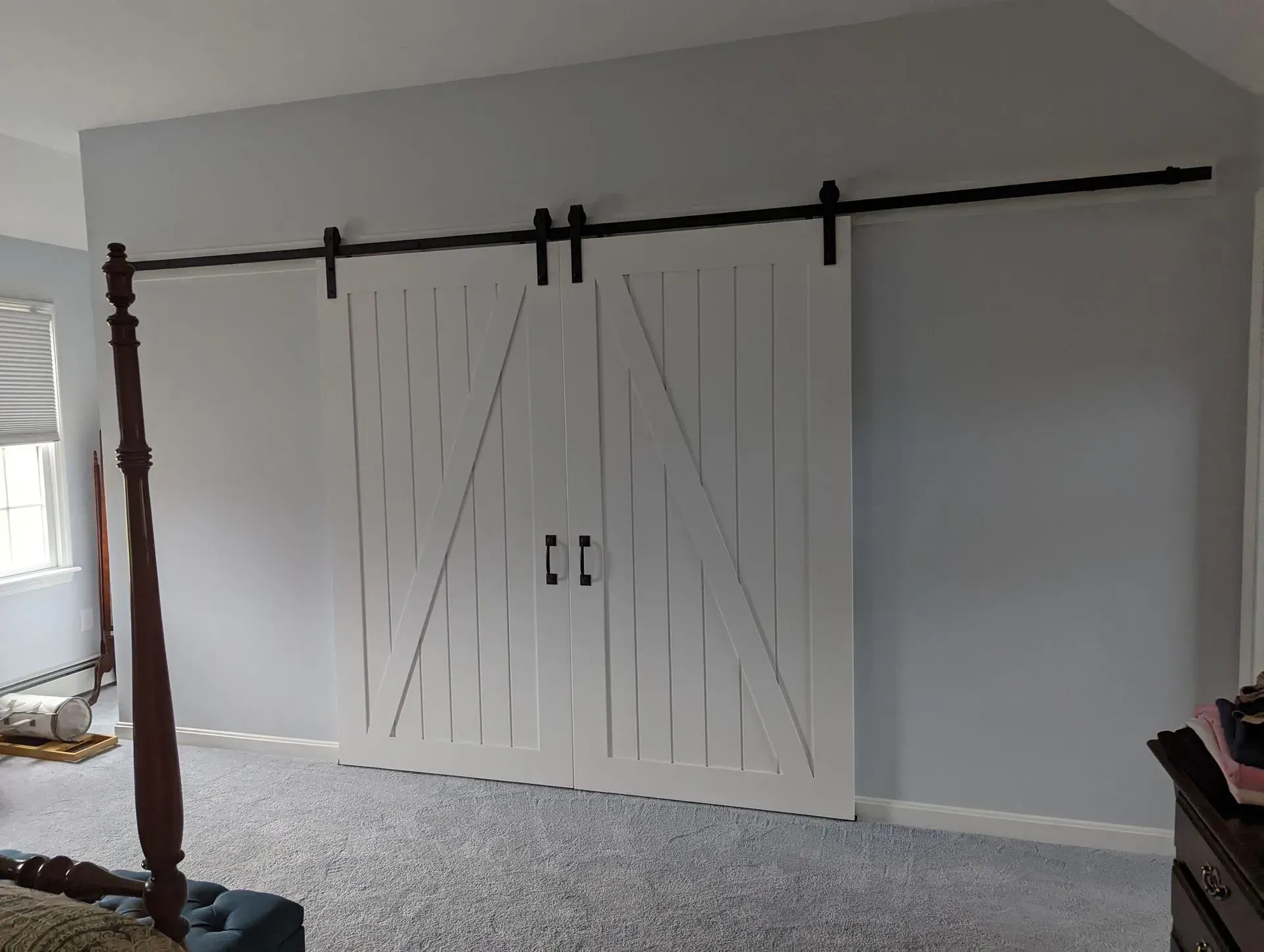 White barn doors on a black sliding track against a gray wall in a carpeted room.