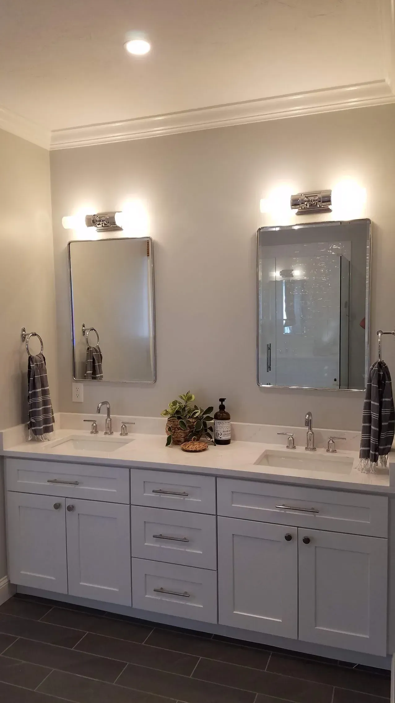 Double vanity bathroom with two mirrors, wall sconces, and white cabinets under a long countertop.