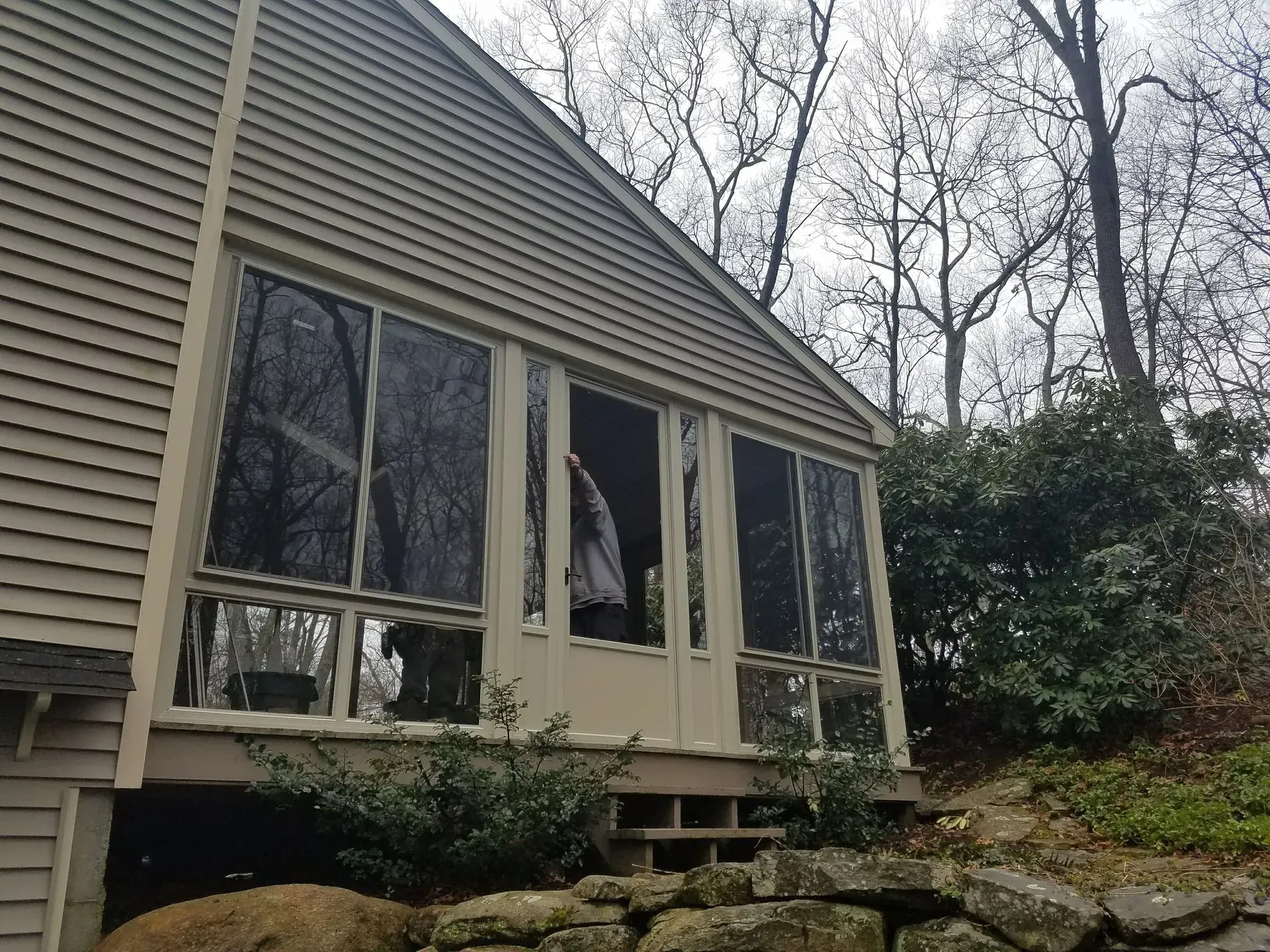 Screened porch on a beige house with wooded yard and stone steps
