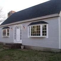 Small gray house with white trim, black roof, and front door with bay windows on a grassy yard