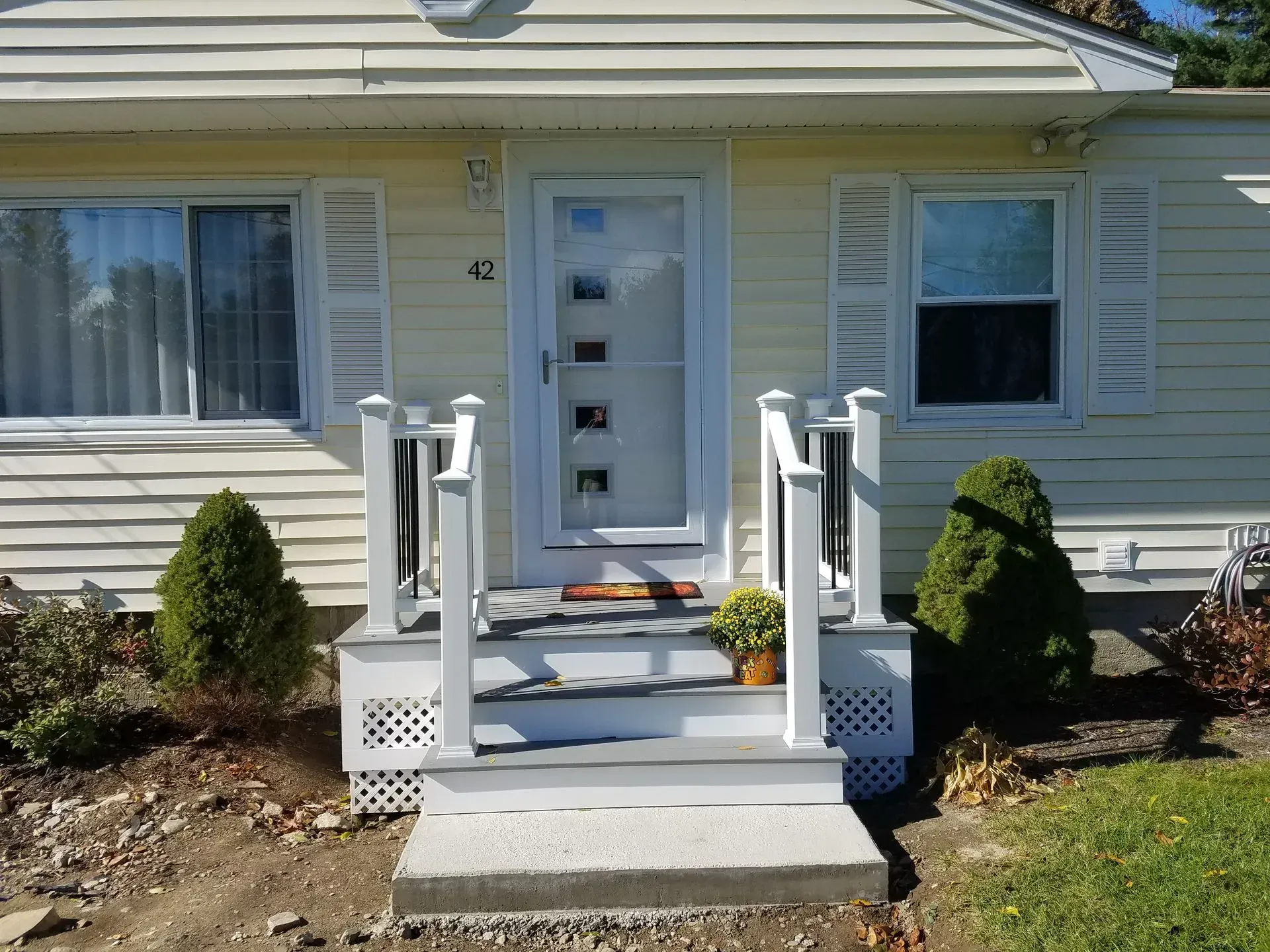 Front entrance of a beige house with white steps, railings, and a white door with small windows