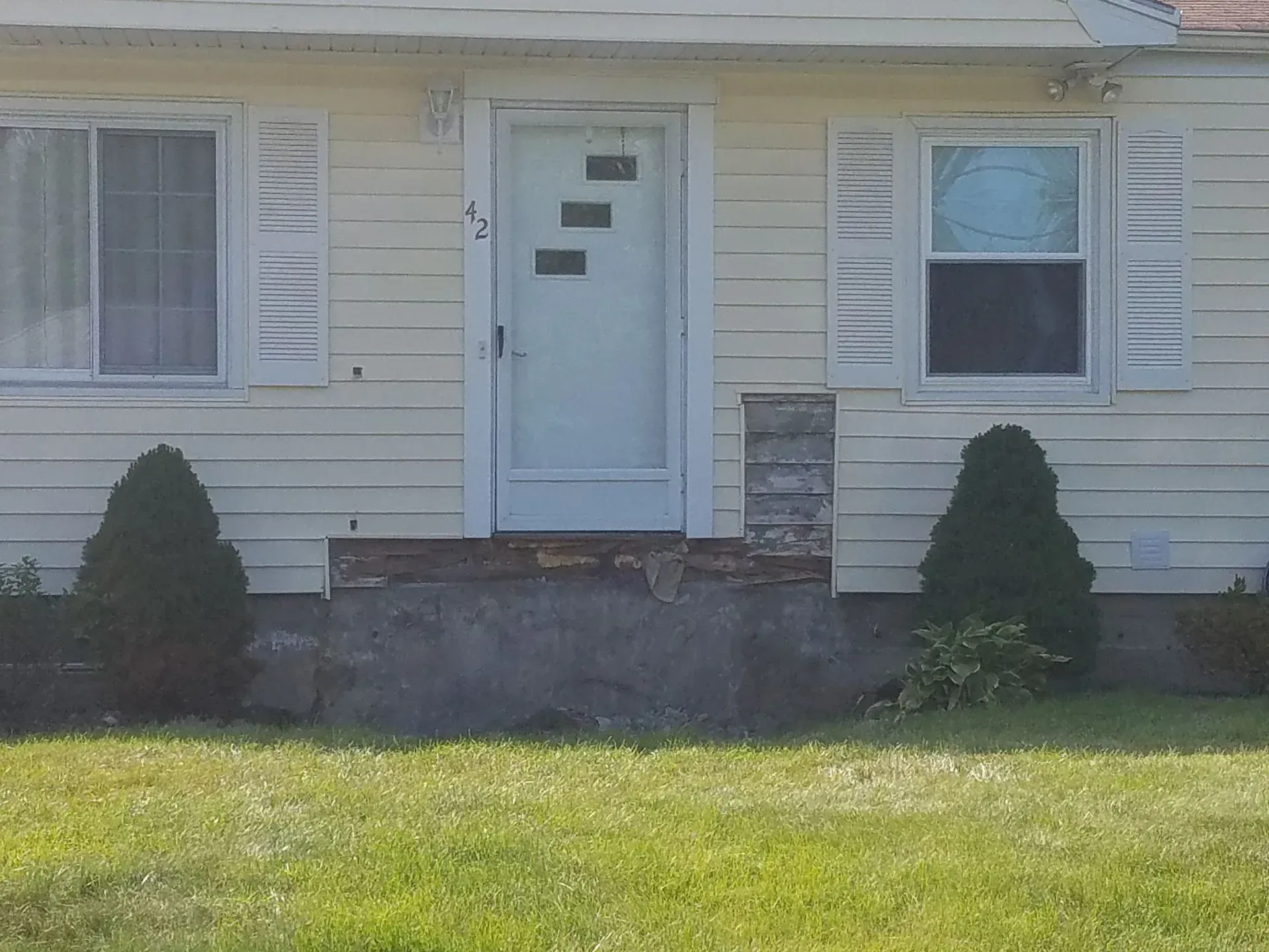 Front view of a beige house with a white door, windows, stone steps, and green lawn.