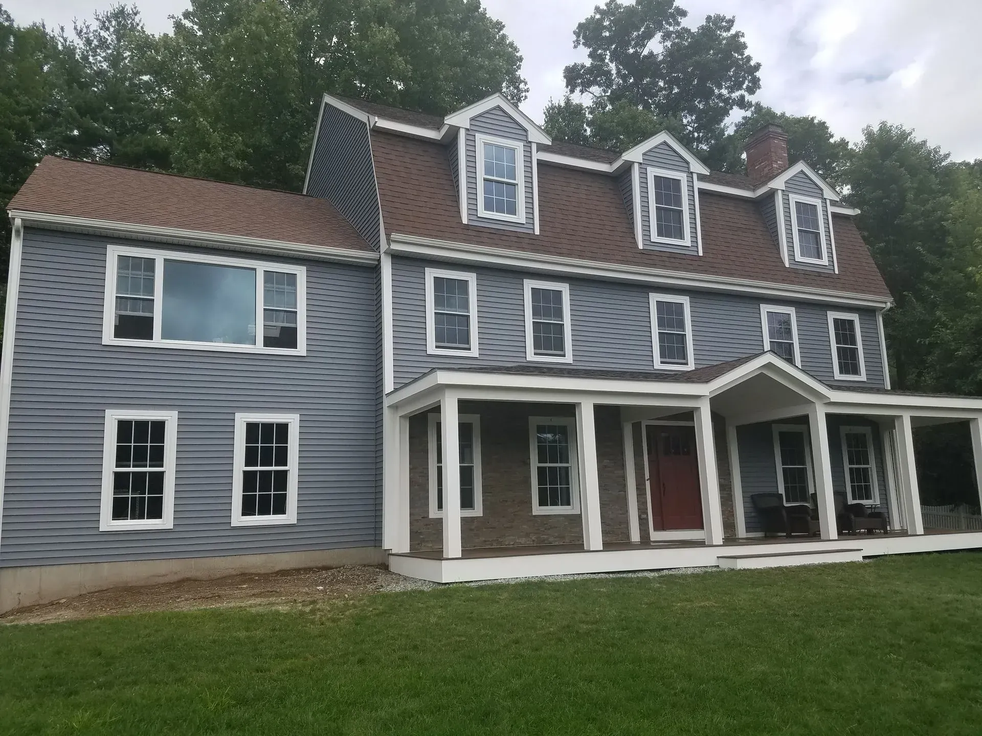 Gray house with white trim, red front door, and a covered porch on a grassy lawn