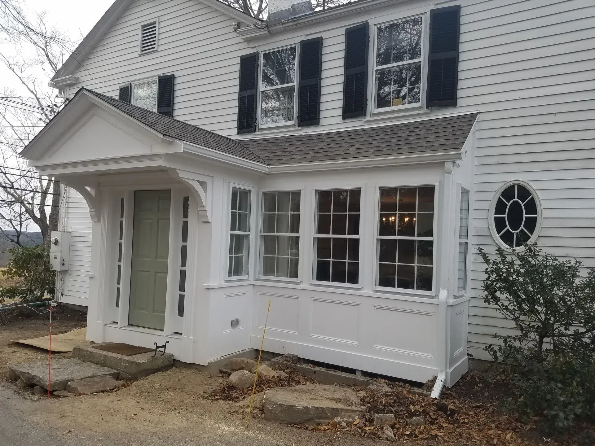 White house exterior with black shutters, front porch, and stone walkway under construction