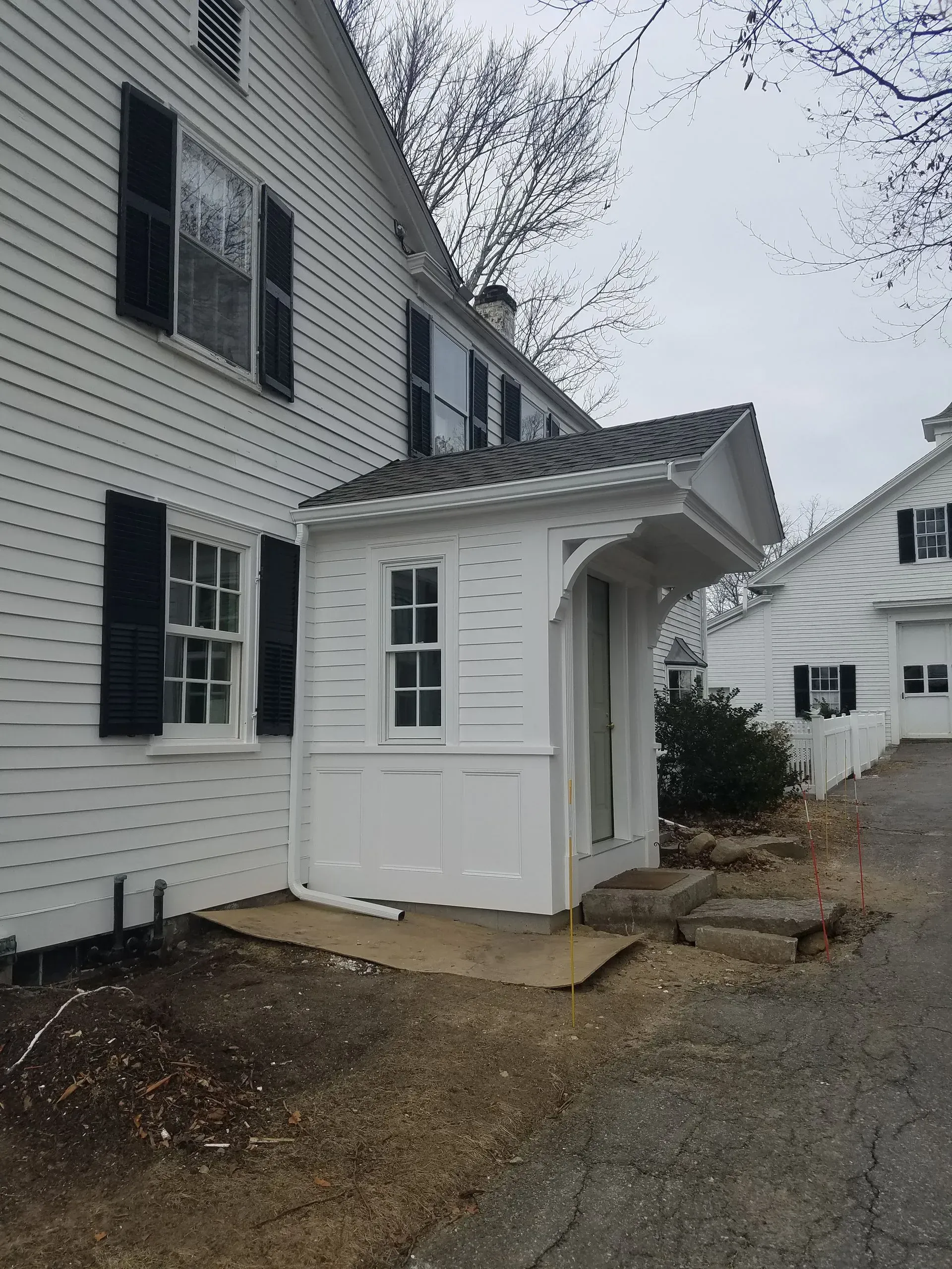 White house exterior with black shutters and a small covered side entrance in a gravel yard