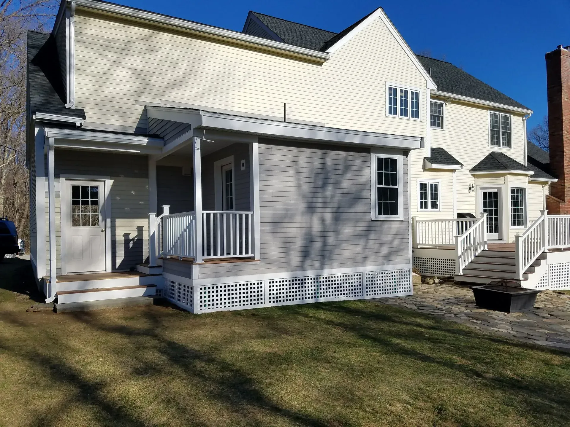 White two-story house with gray siding, porches, and a sunlit lawn