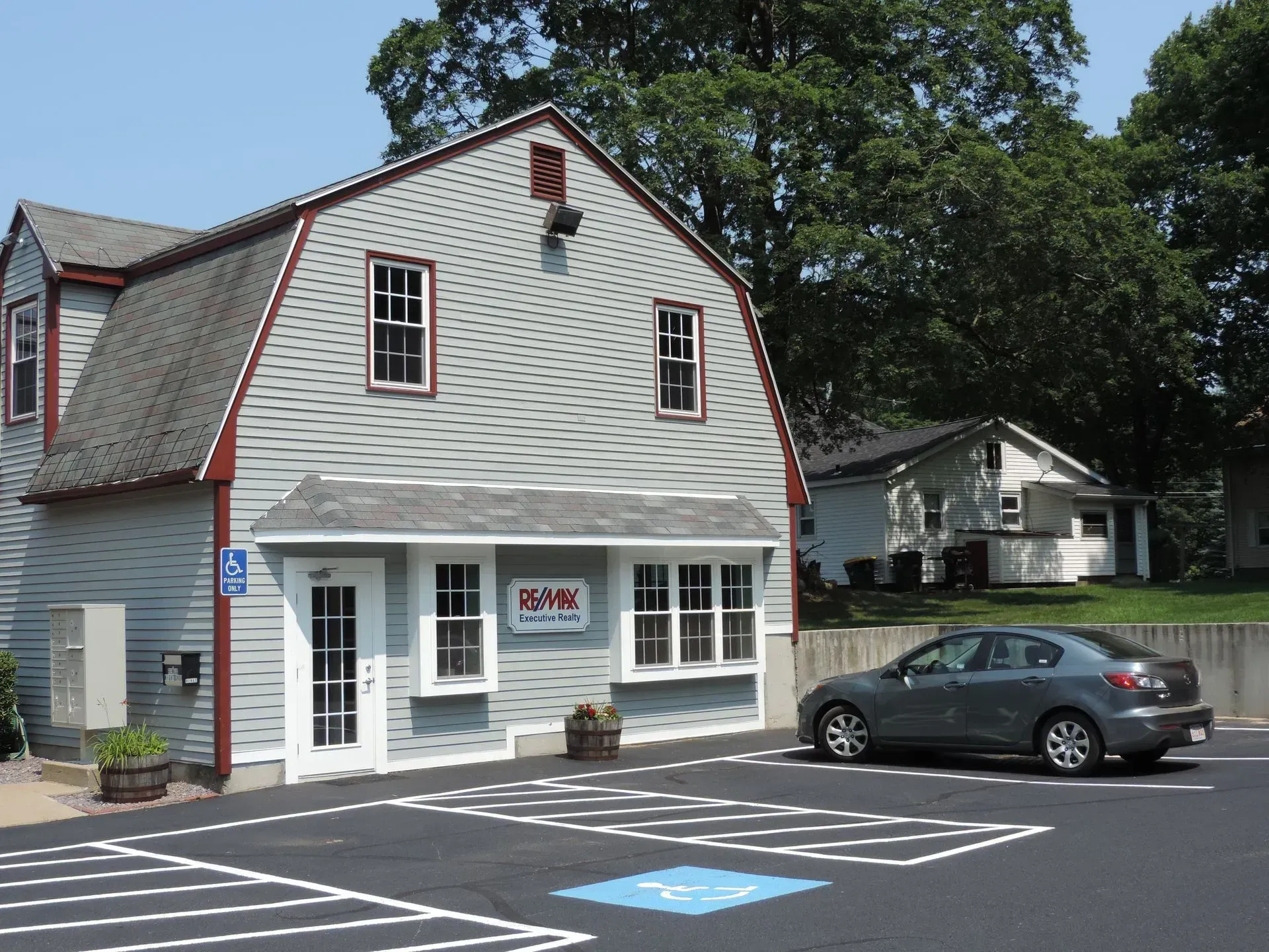 Small white storefront with red trim and a parked gray car in a lot with accessible parking space markings