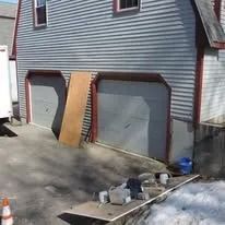 Two-car garage with a ramped plywood board between the doors and tools scattered on the driveway.
