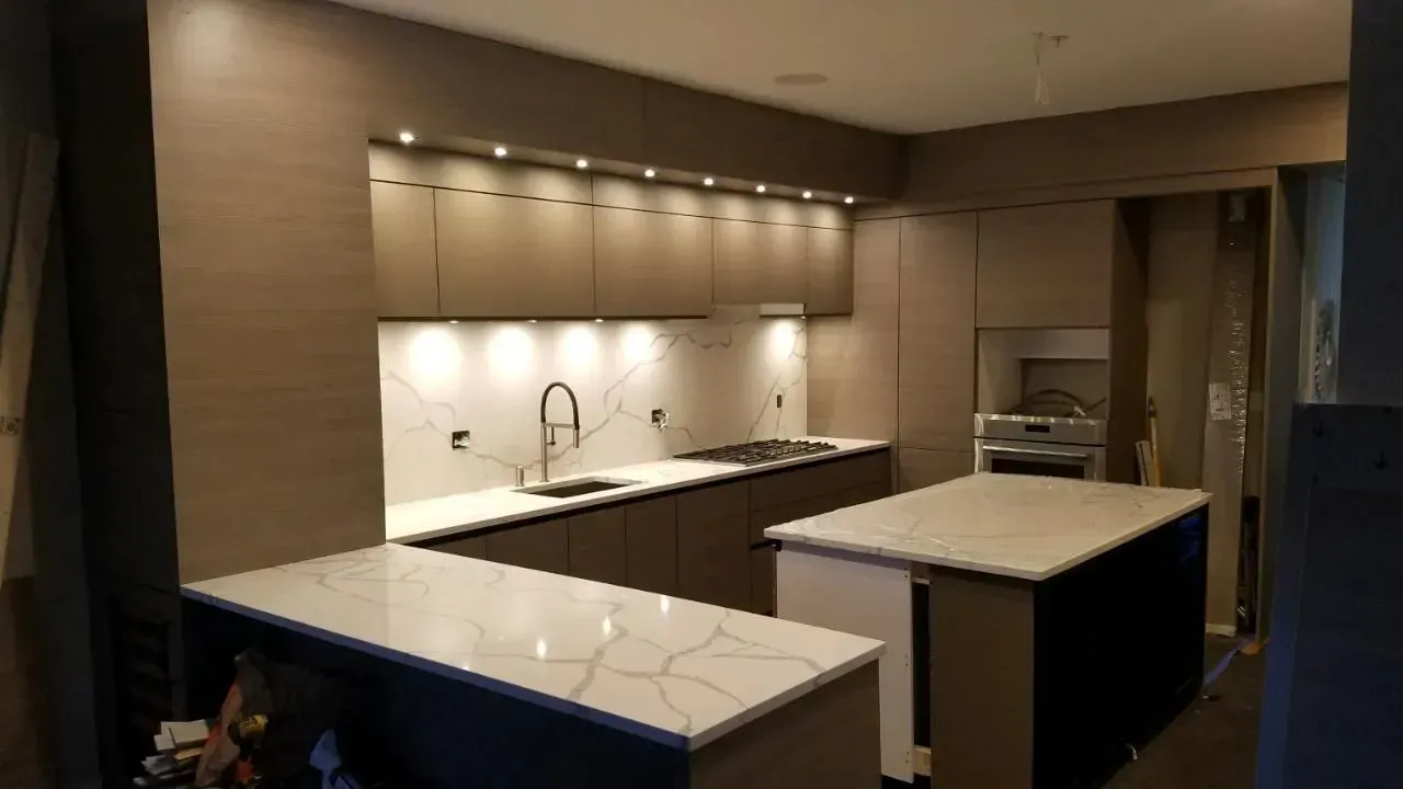 Modern kitchen with white countertops, built-in cabinets, and warm under-cabinet lighting in a dim room