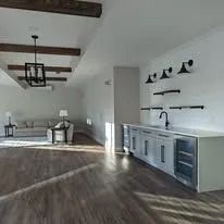 Bright modern open-plan room with wood floors, exposed beams, and a long built-in cabinet wall