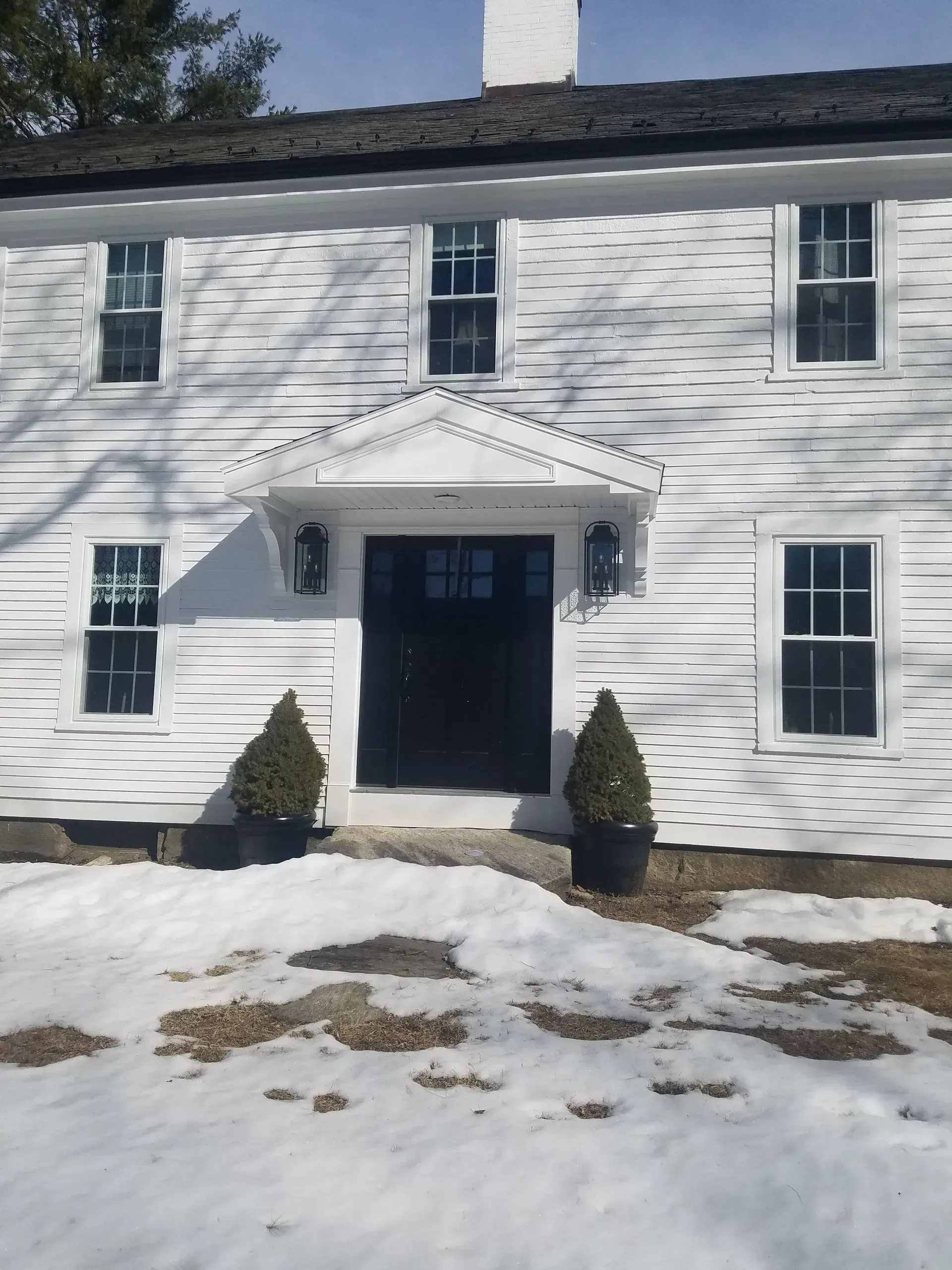 Snow-covered white house with black trim and a dark front door
