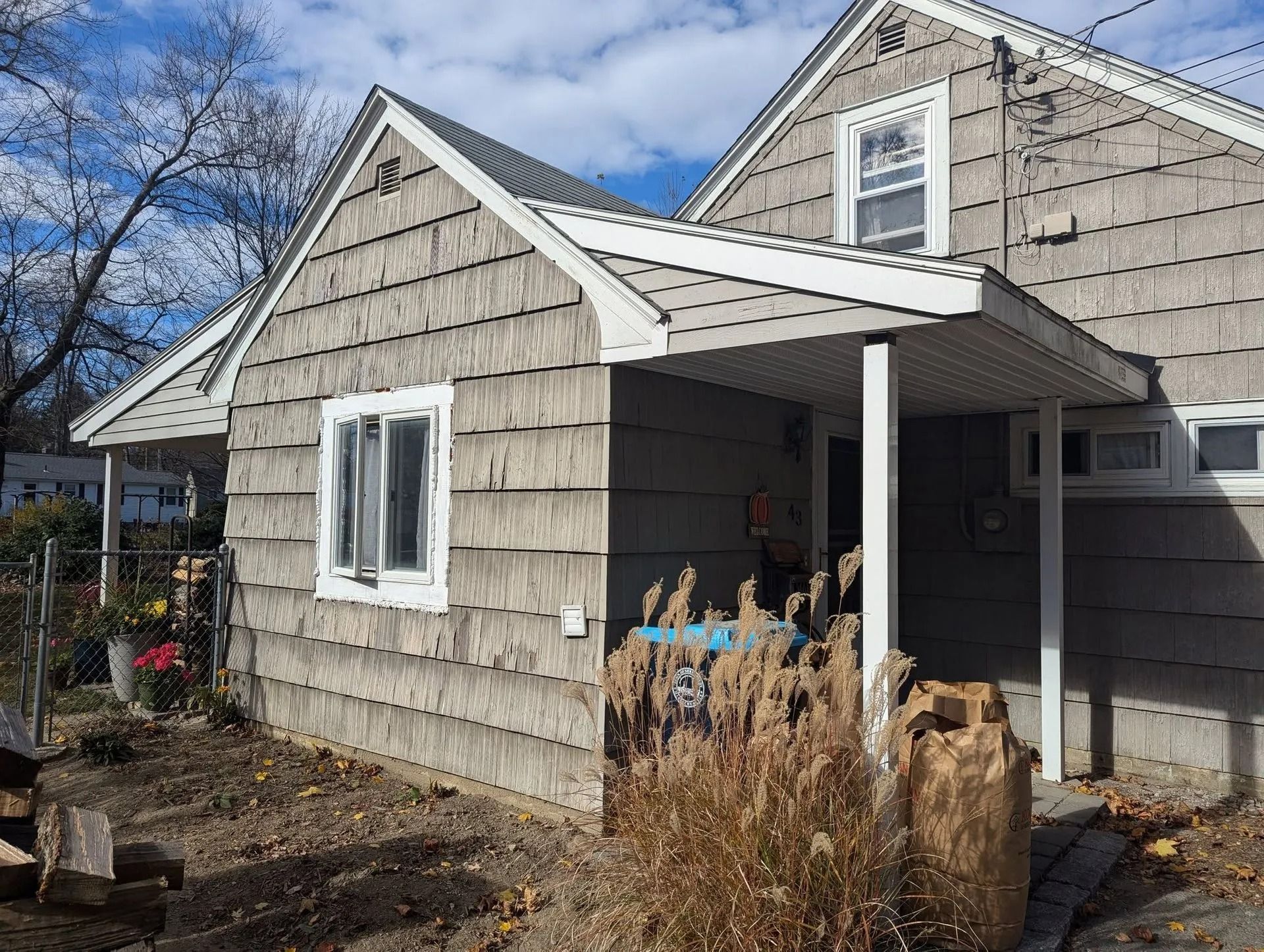 Small gray house with white trim and porch, viewed from the side on a sunny day.