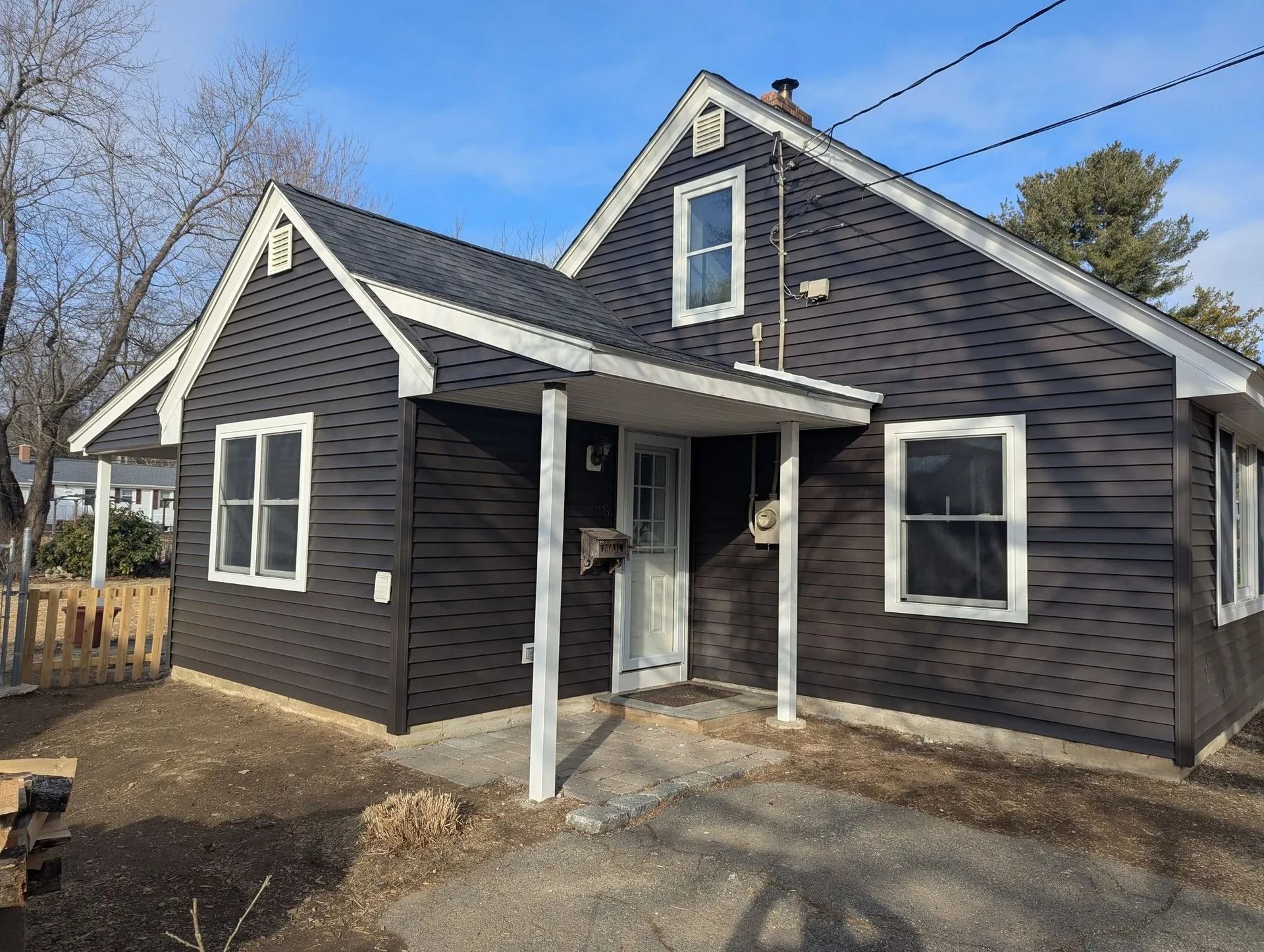 Small dark house with white trim and a front porch in a yard under a blue sky