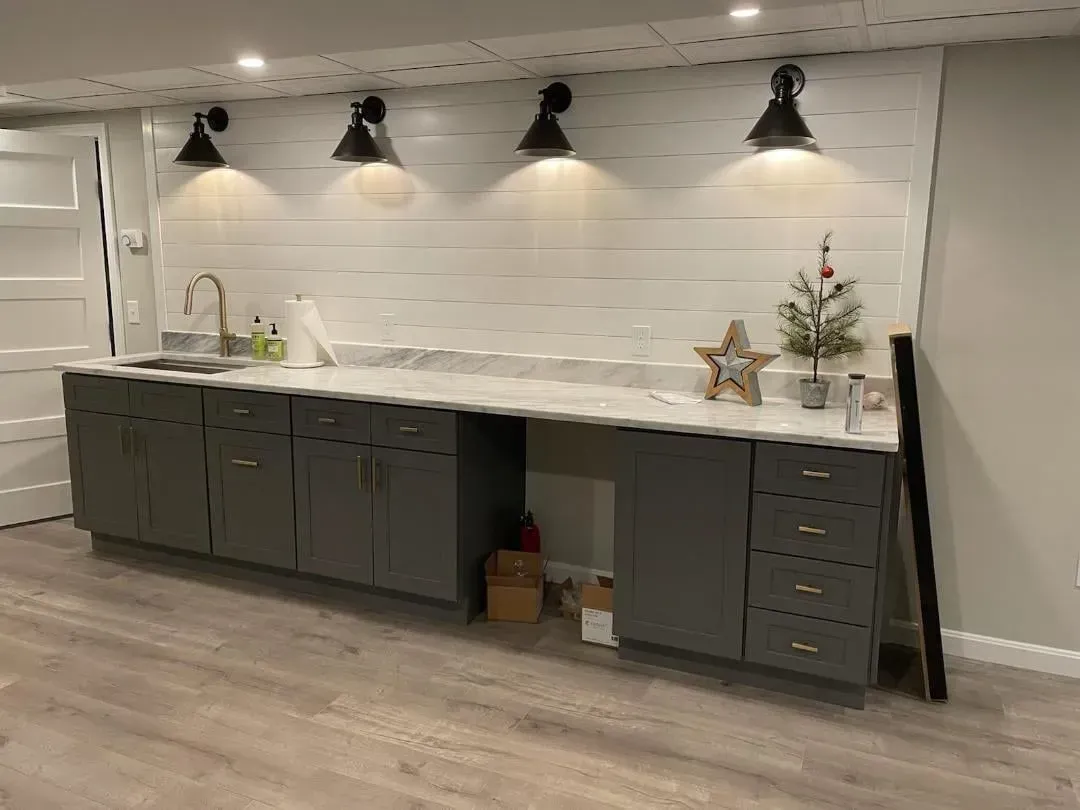 Modern kitchen with dark cabinets, white backsplash, countertop lights, and wood-look flooring