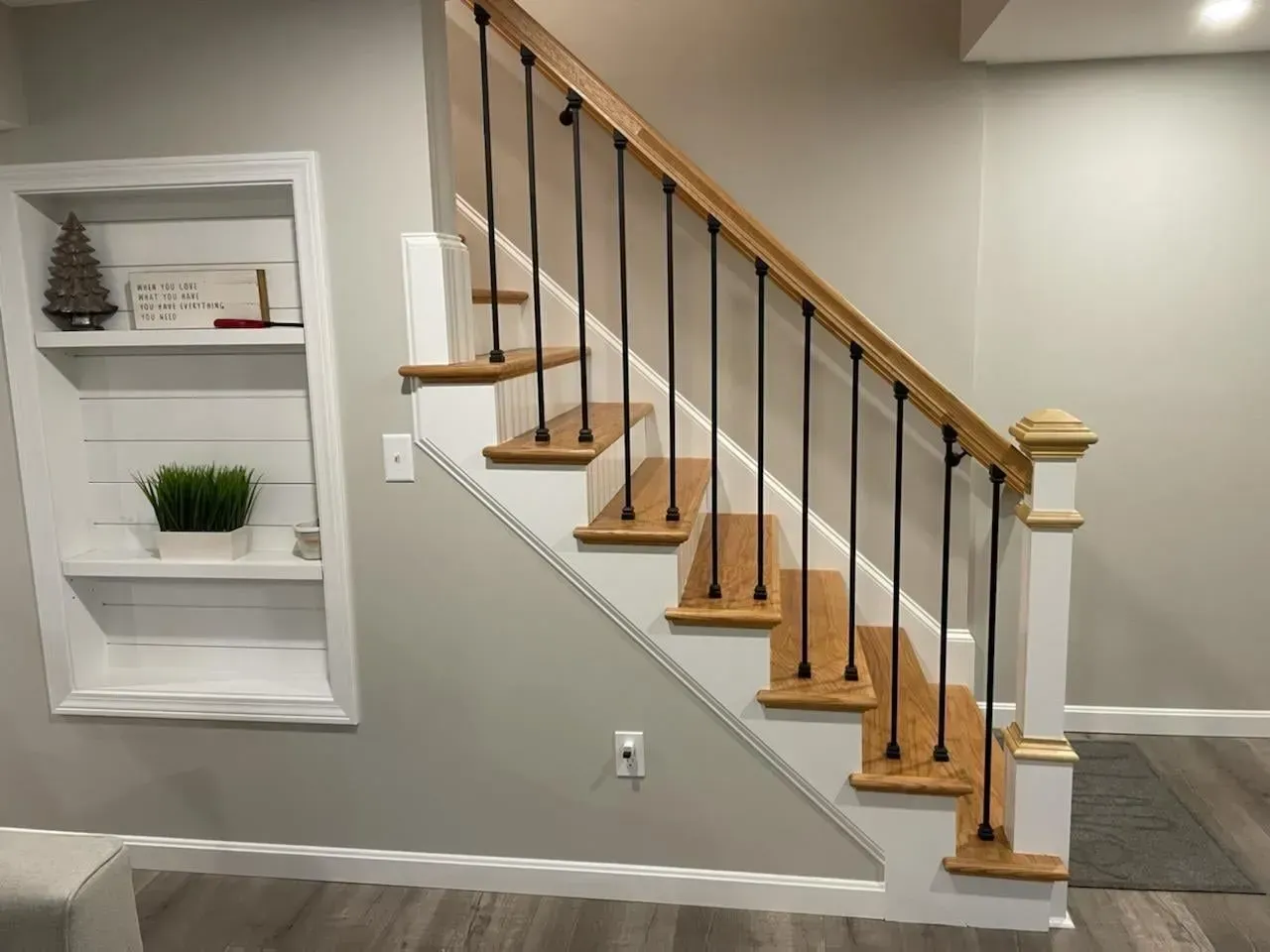 Indoor staircase with wooden steps, black railings, and a small wall shelf display in a light gray room
