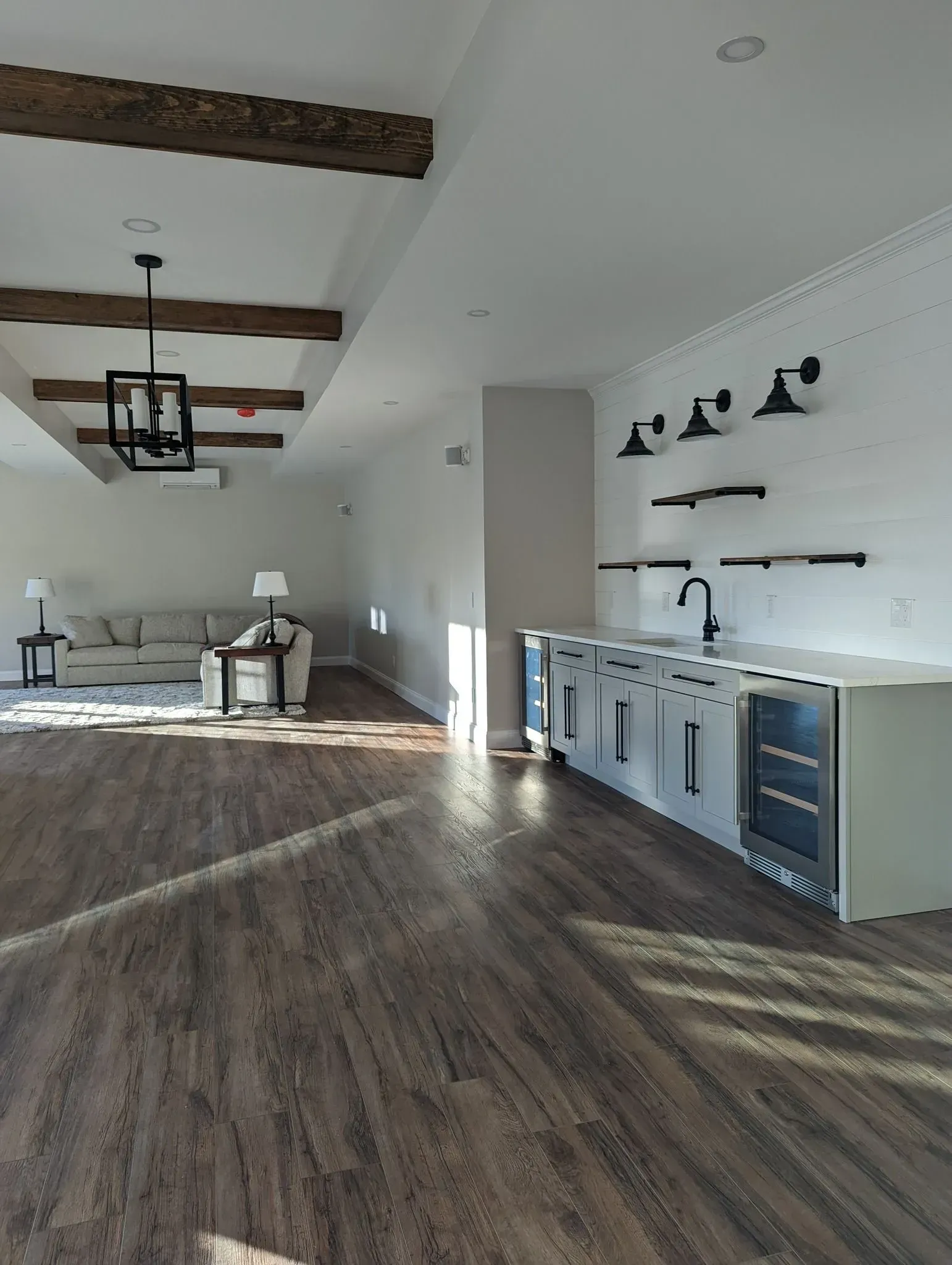 Modern open living room with rustic beams, wood floors, and a white kitchen with a bar and stools