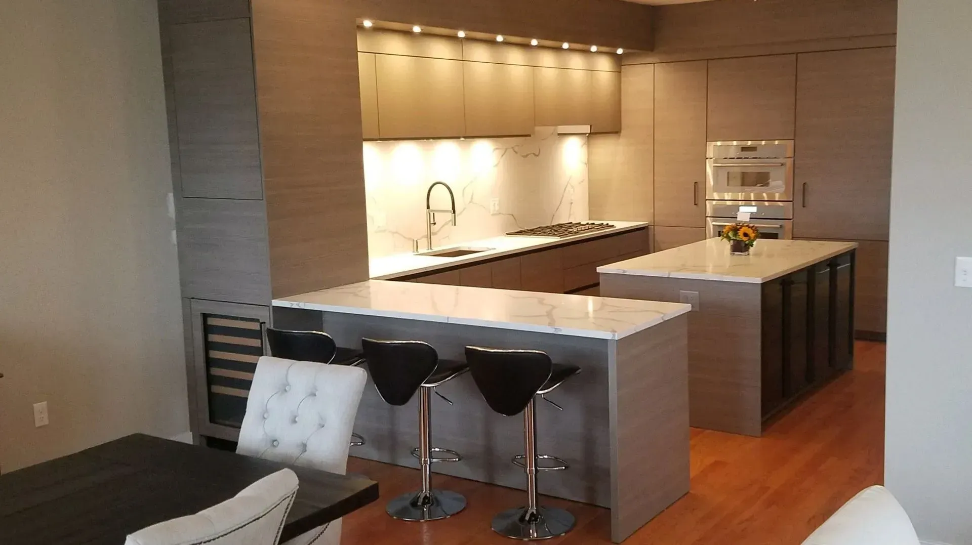 Modern kitchen with island seating, white cabinets, and stainless steel appliances, viewed from the living room.