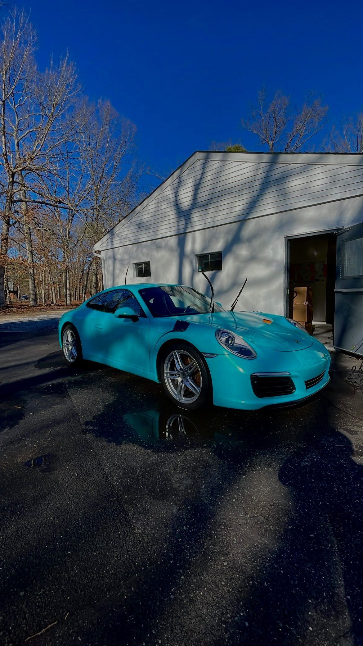 Turquoise sports car parked beside a white garage under a clear blue sky