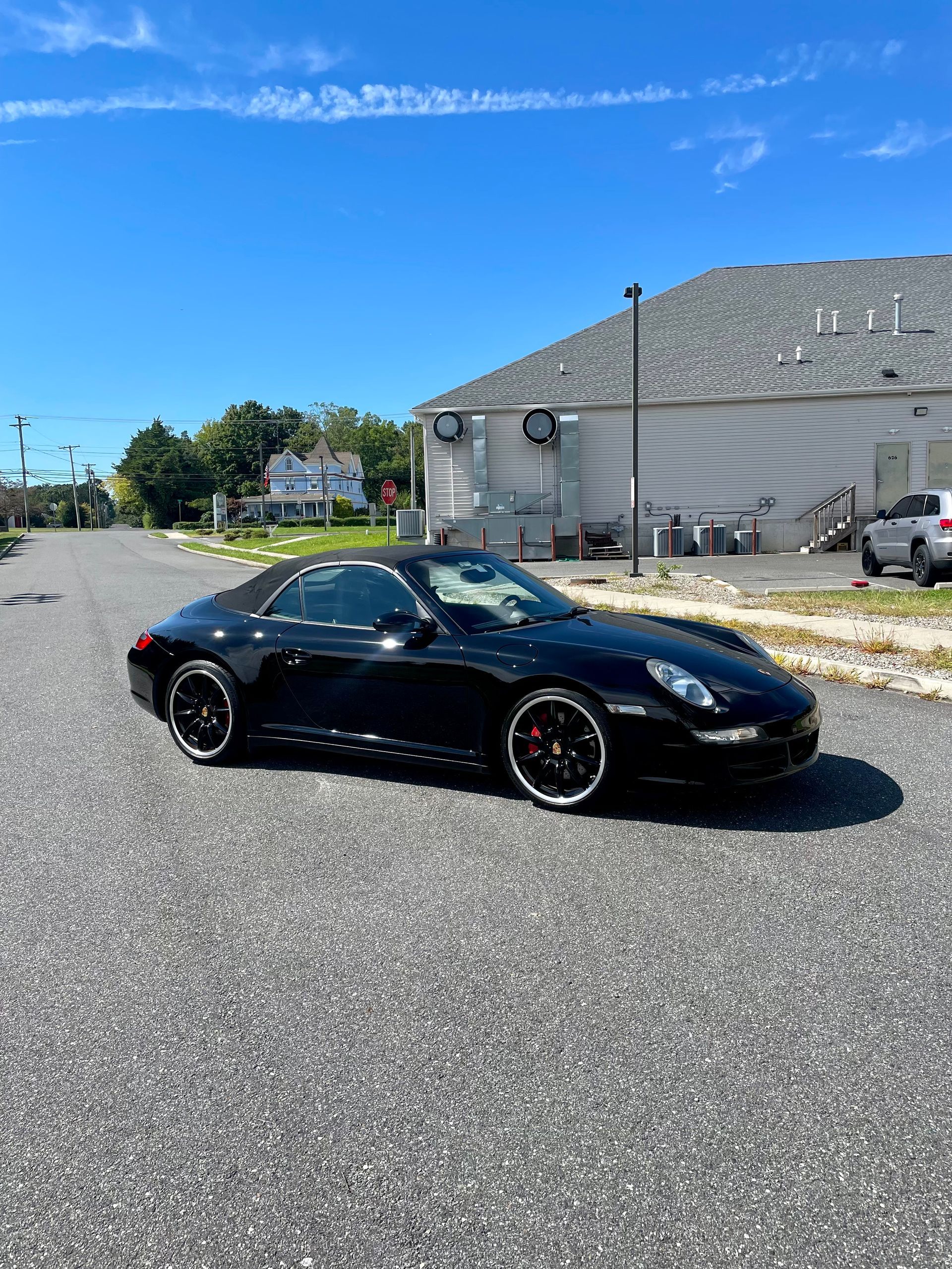Black sports car parked on a sunny gravel lot beside a gray building under a blue sky