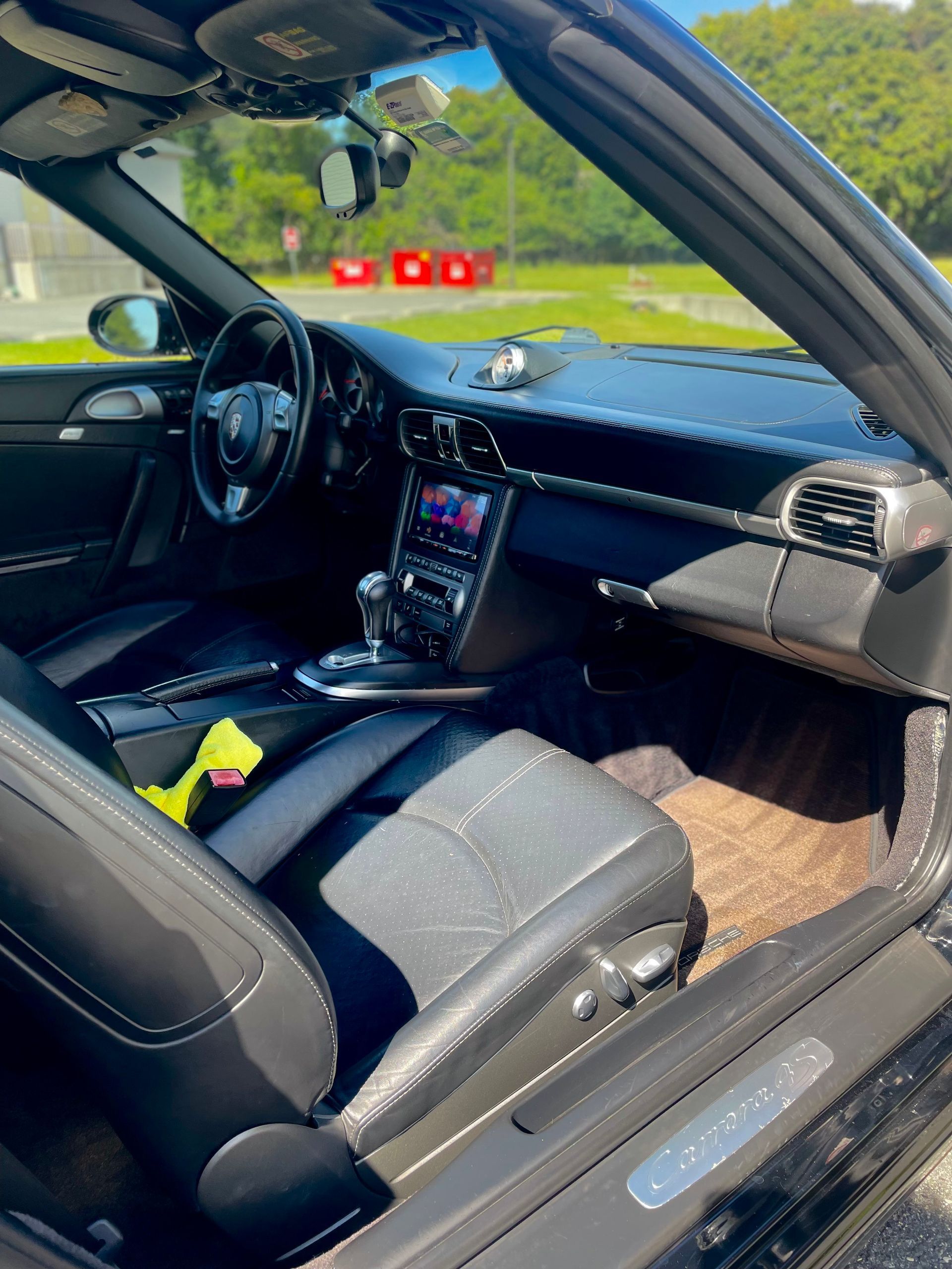 Black car interior with open door, steering wheel, center console, and visible tan floor mats.