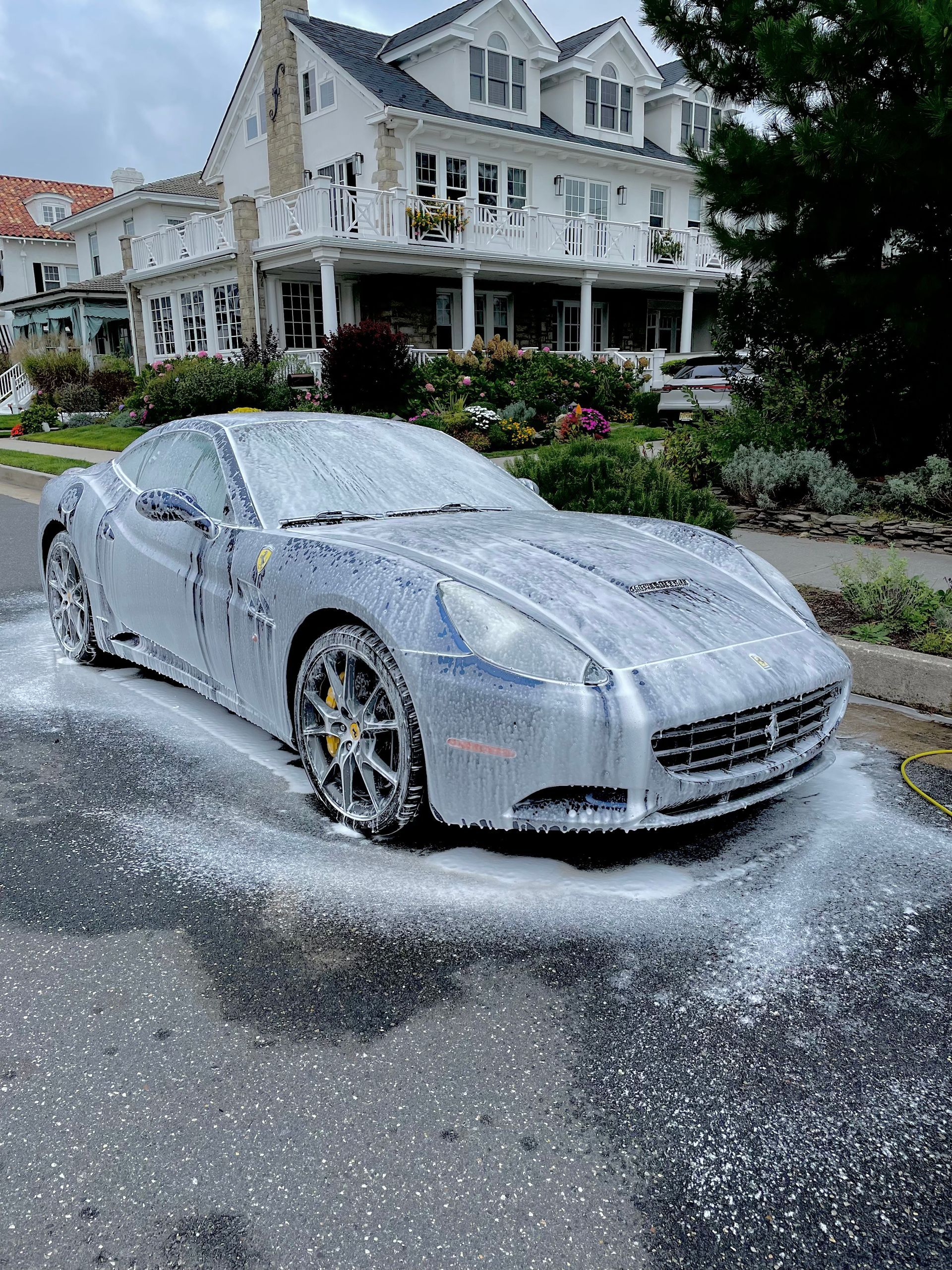 Silver sports car driving through soapy foam in front of a large white house