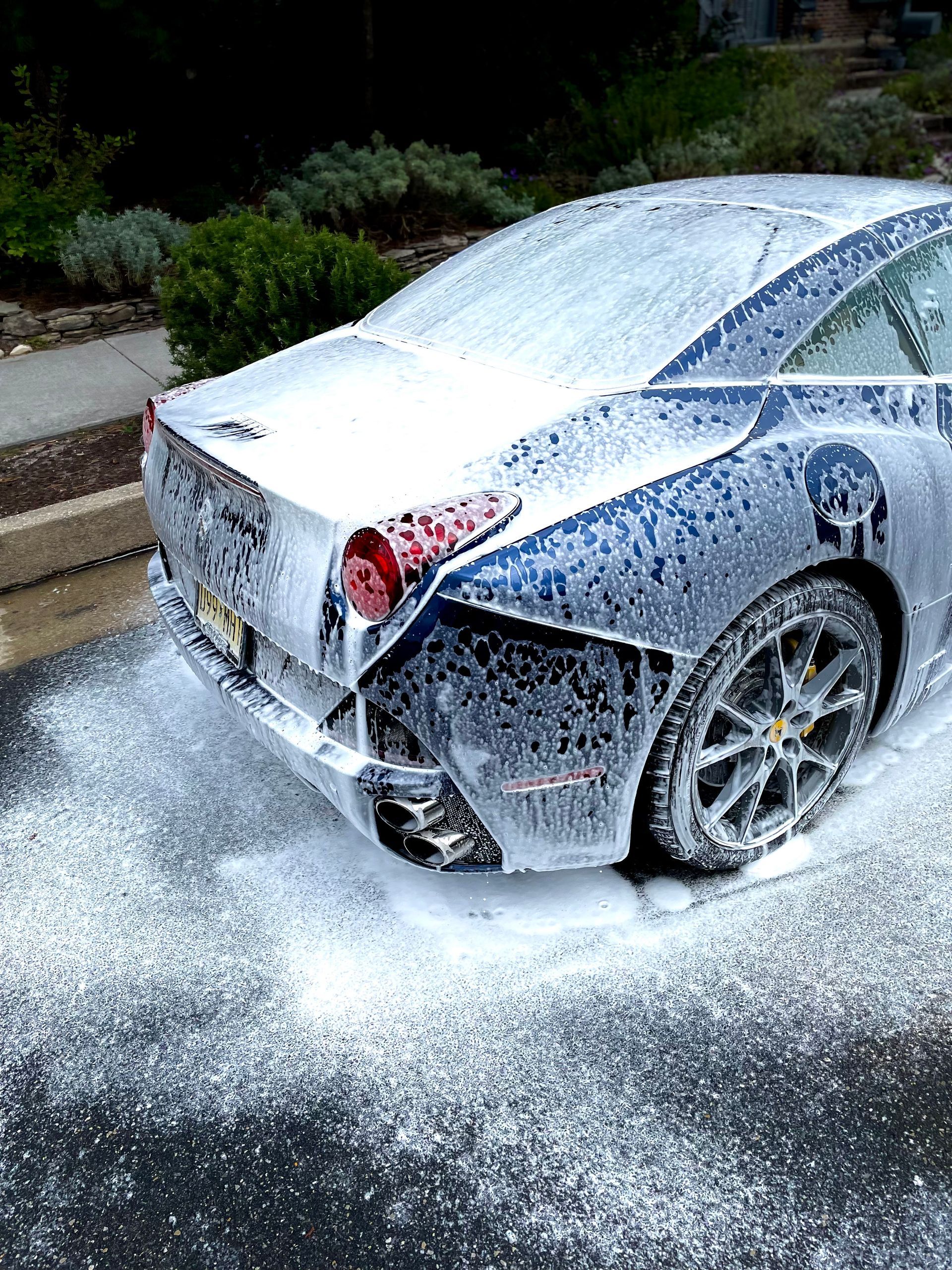 Silver sports car being covered in white foam during a wash on a driveway