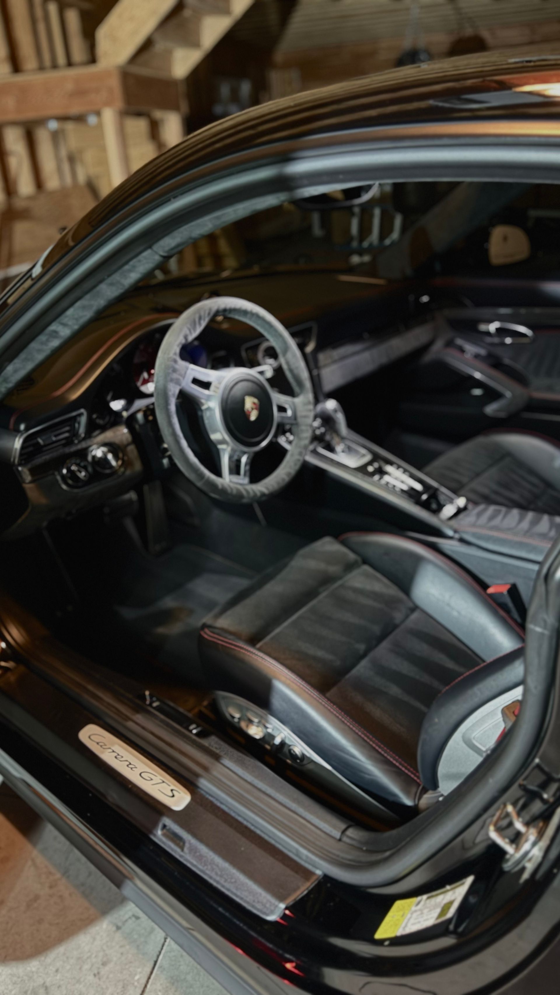 Black sports car interior with open door, showing steering wheel and black leather seats.