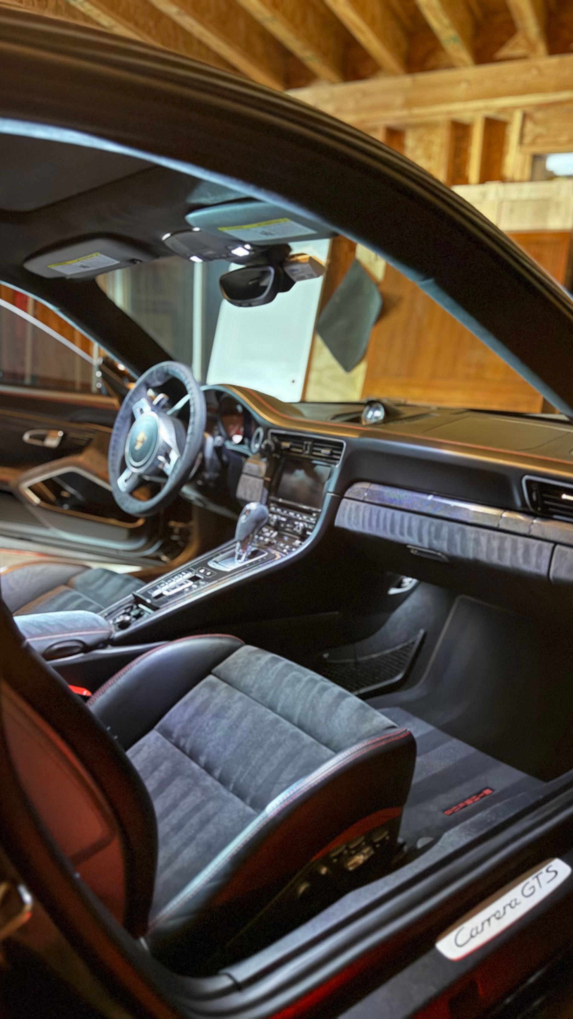 Interior of a black sports car with a steering wheel, center console, and bucket seats in a garage