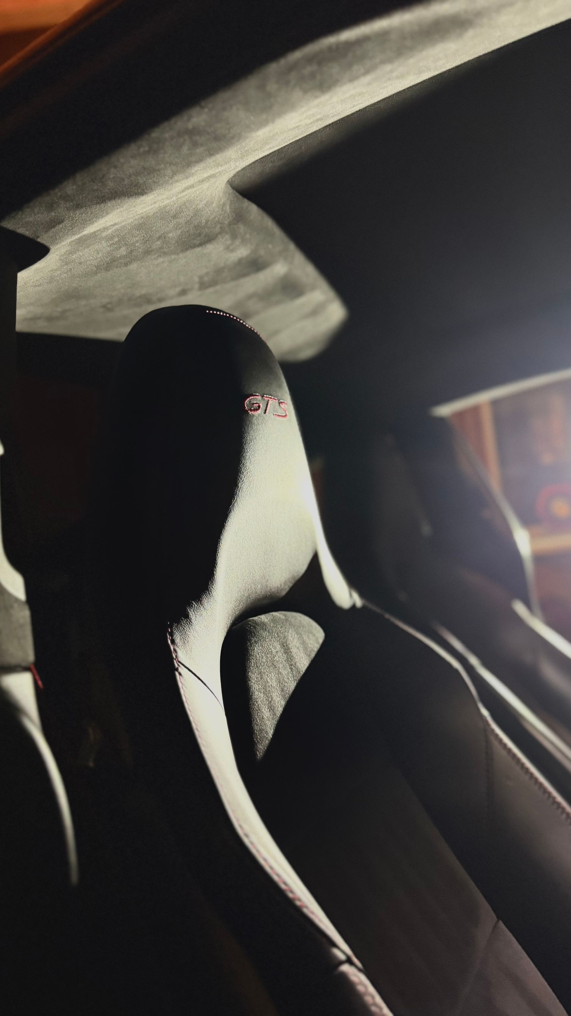 Black-and-white racing seat with harness in a car interior, lit by sunlight