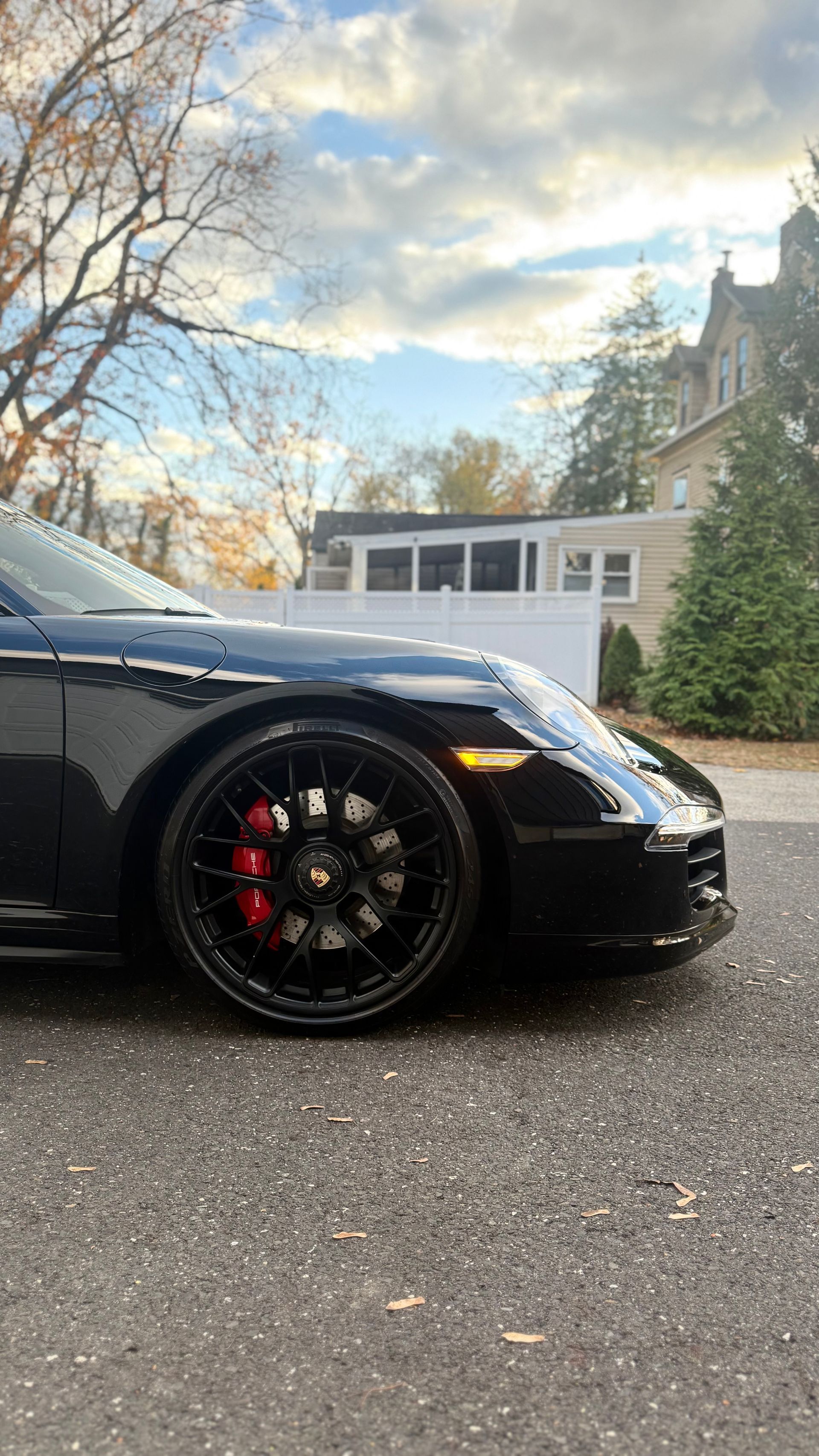 Black sports car parked in a driveway, side view with red brake calipers and a house in the background
