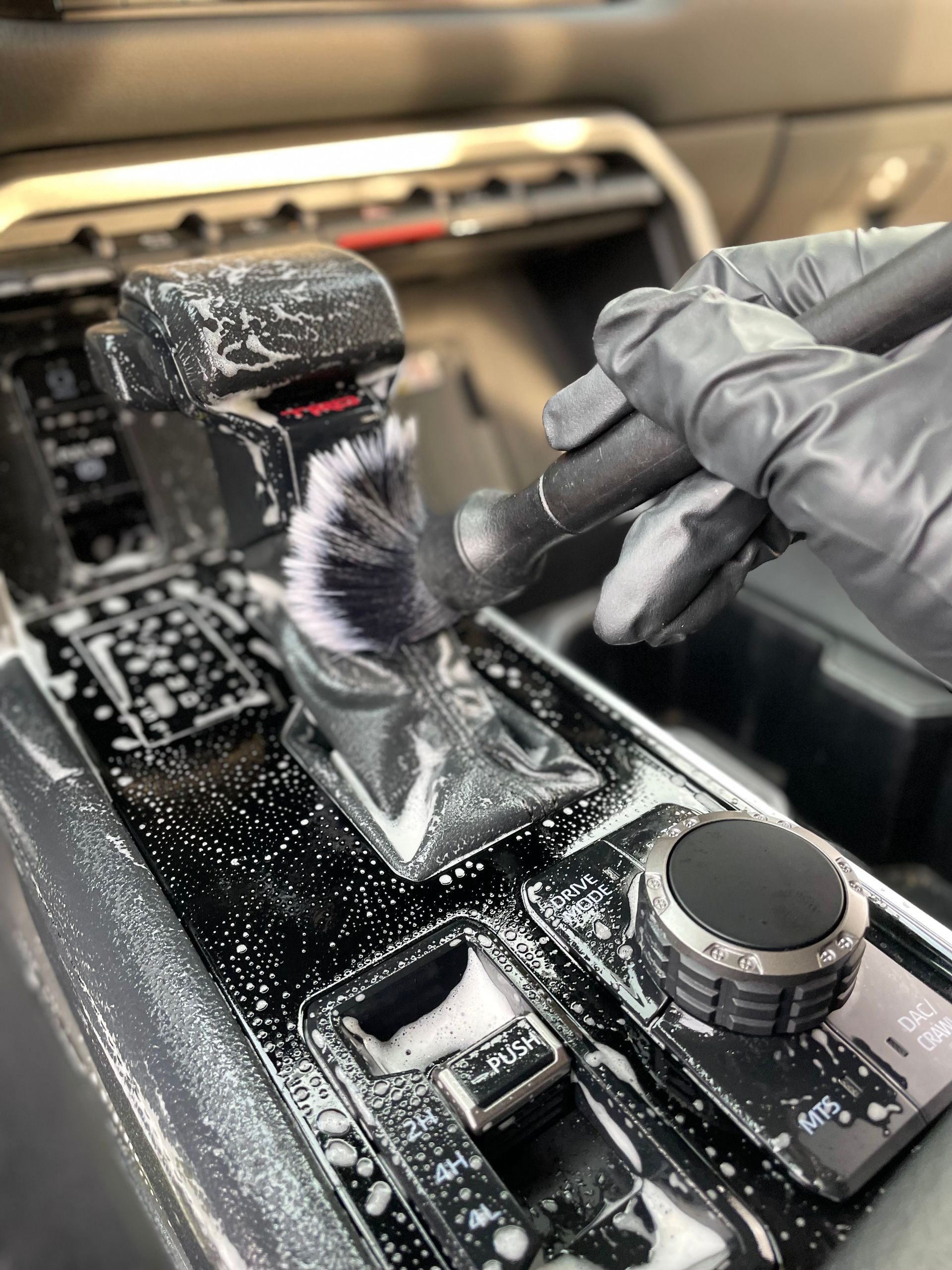 Gloved hands cleaning a car’s gear shifter and center console with a brush