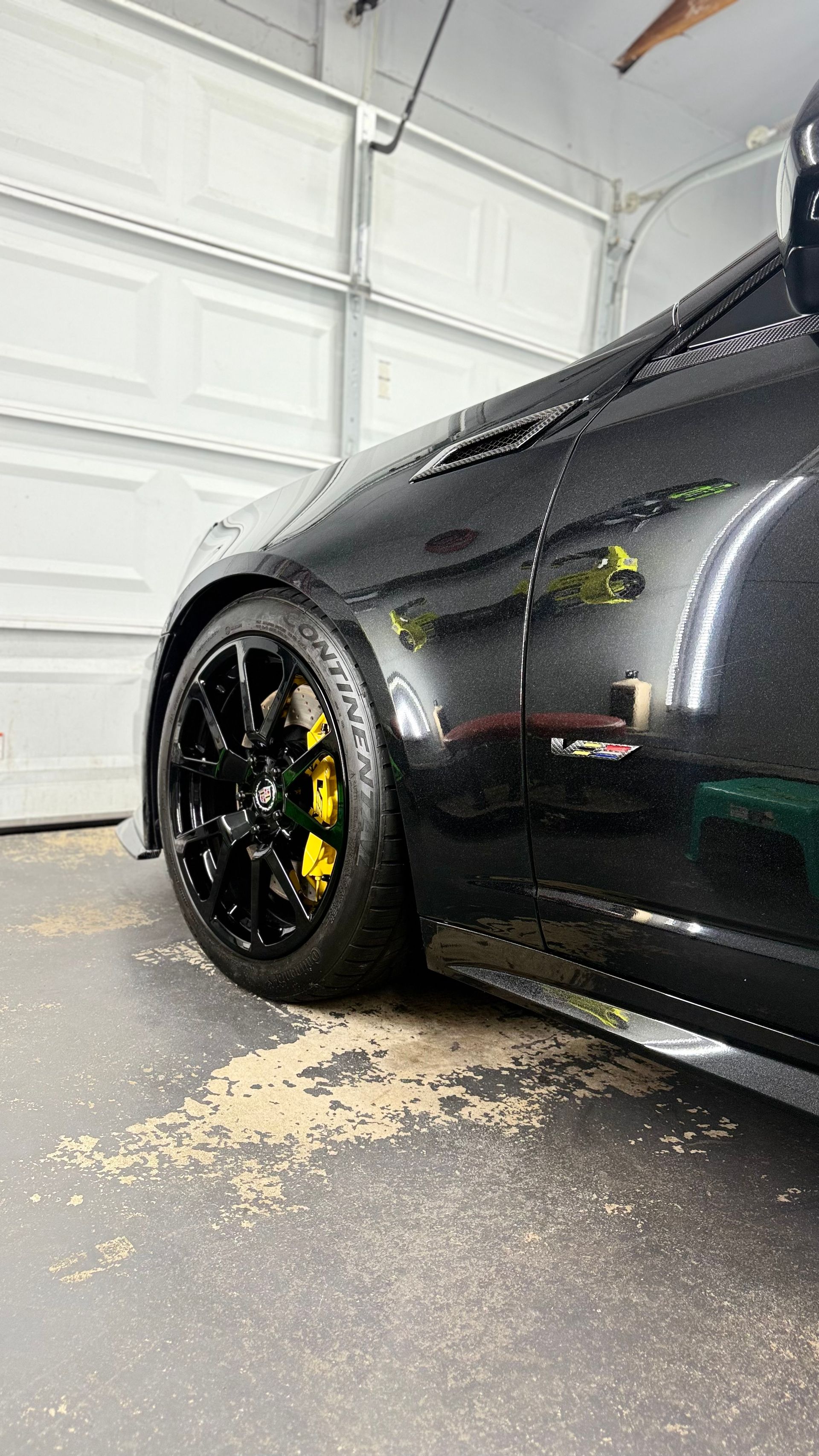Black sports car with yellow brake calipers parked in a garage, with spilled material on the floor.