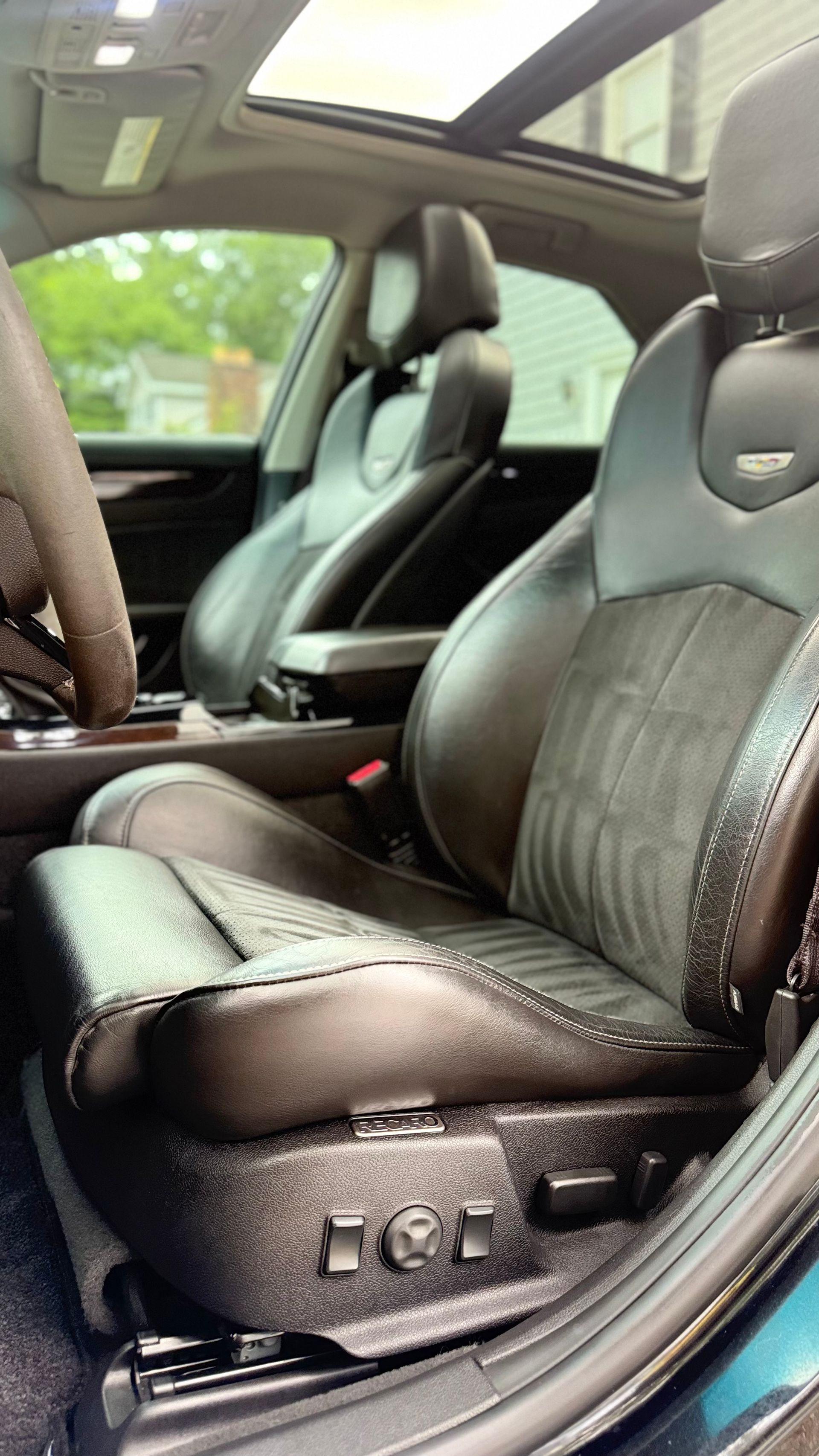 Luxury car interior with black leather front seats and panoramic sunroof, viewed from the passenger side