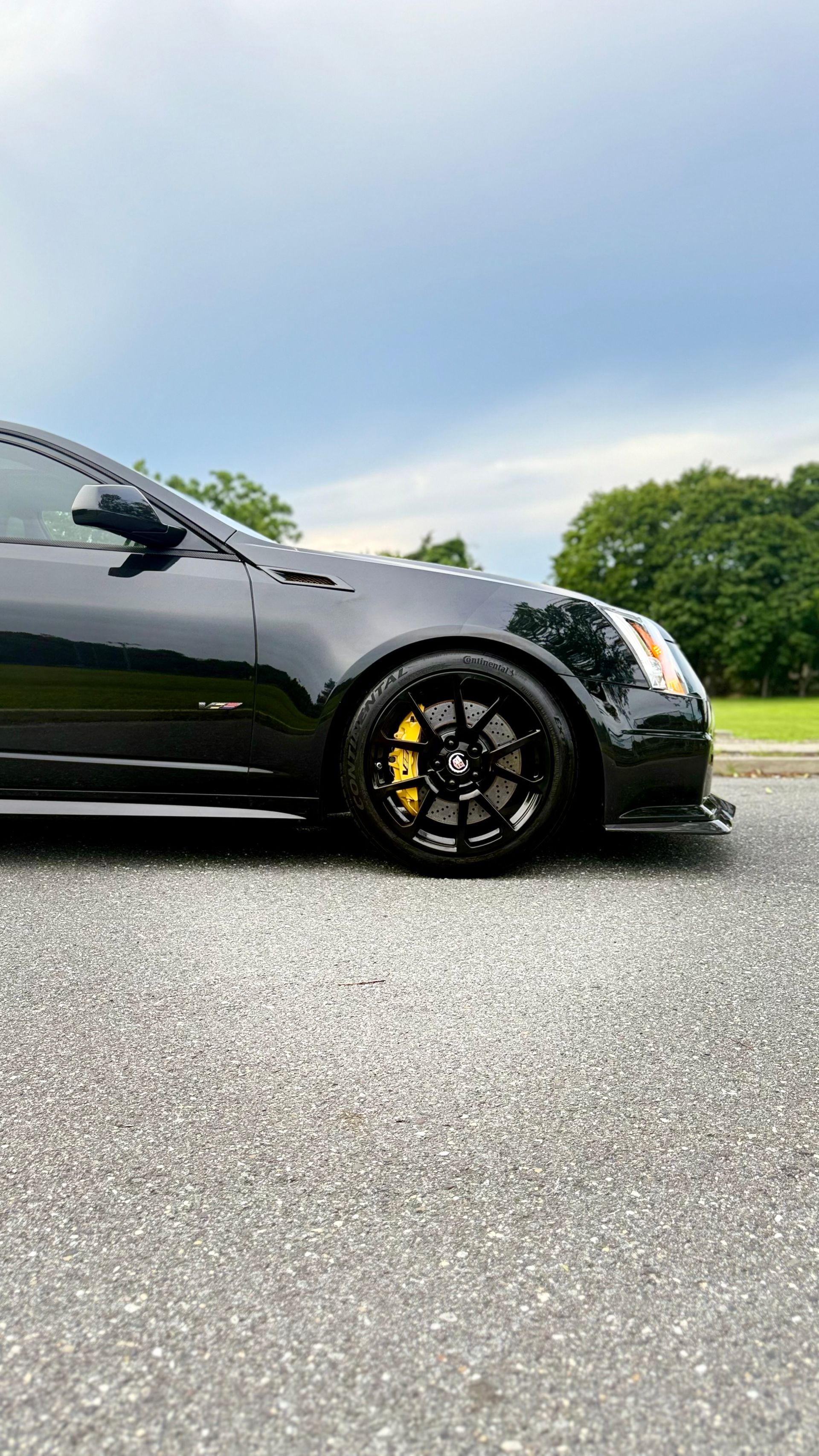 Black sports car parked on wet pavement under a cloudy sky, side view with yellow brake calipers