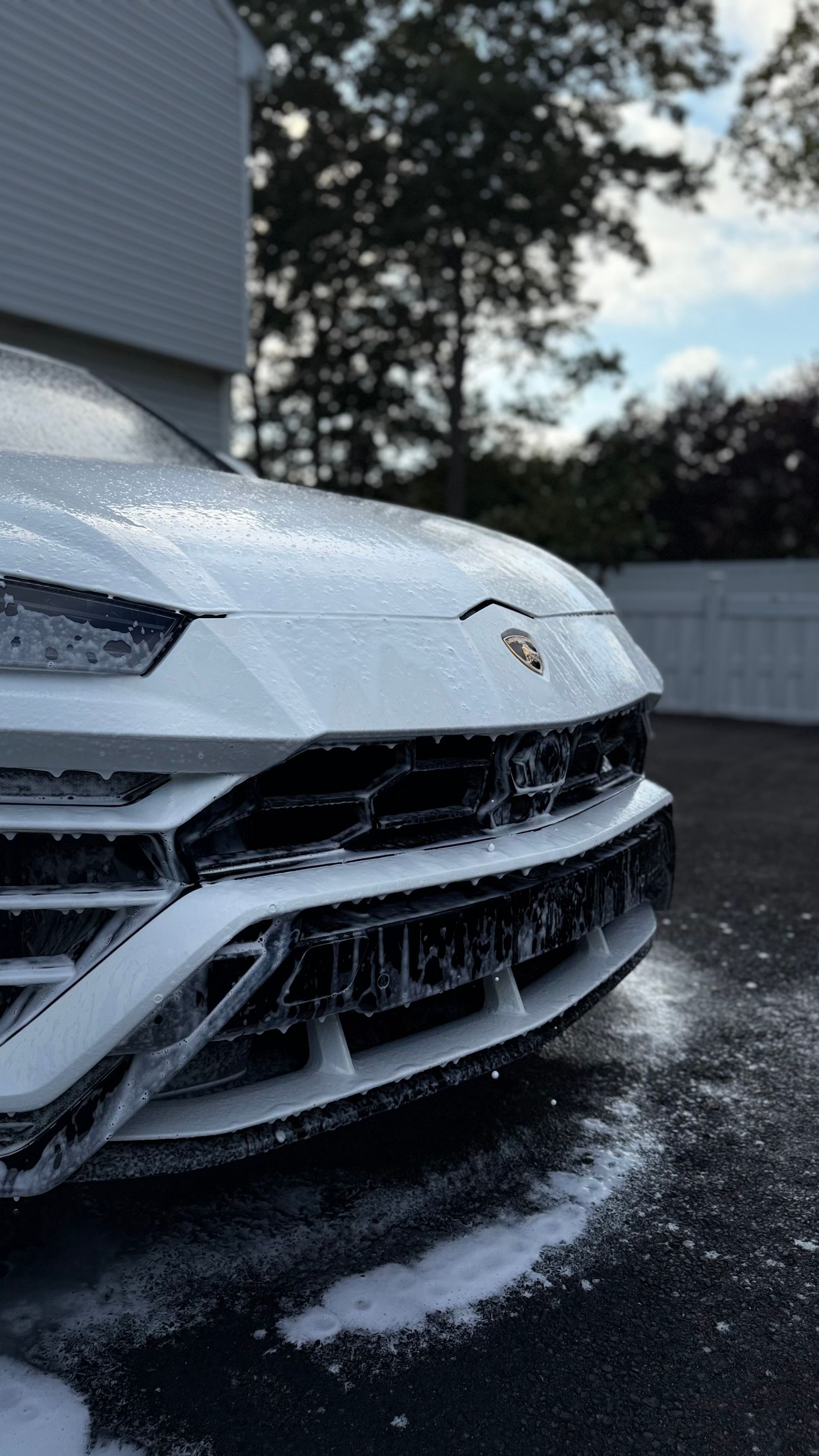 White sports car front bumper splashing through water on a wet driveway or road