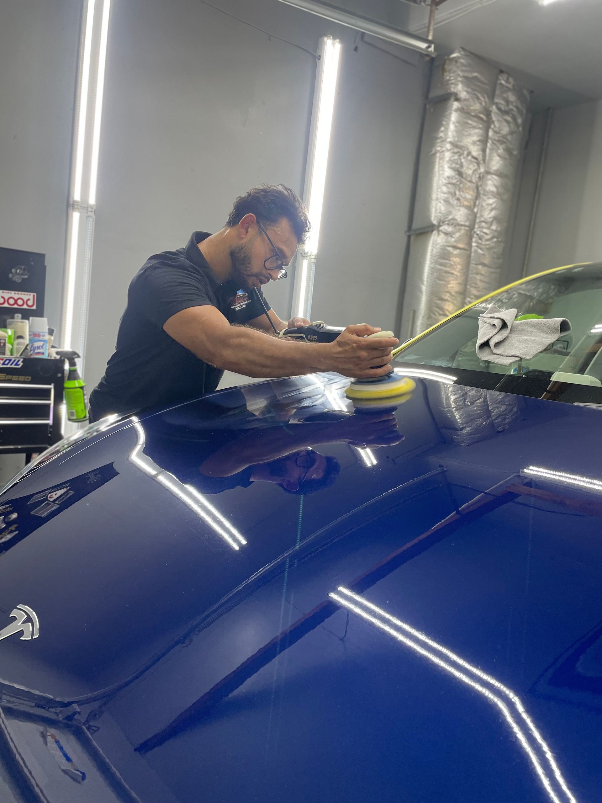 Person polishing a blue car in a workshop under bright overhead lights