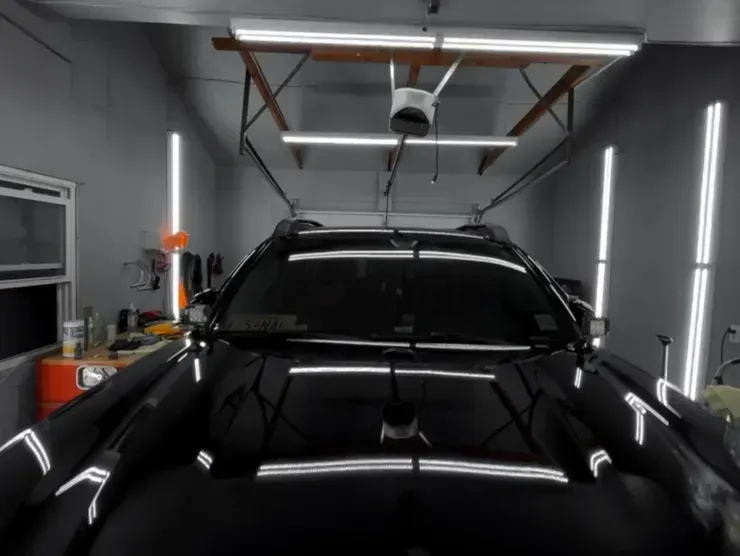 Black car in a modern garage with bright overhead and wall lights.