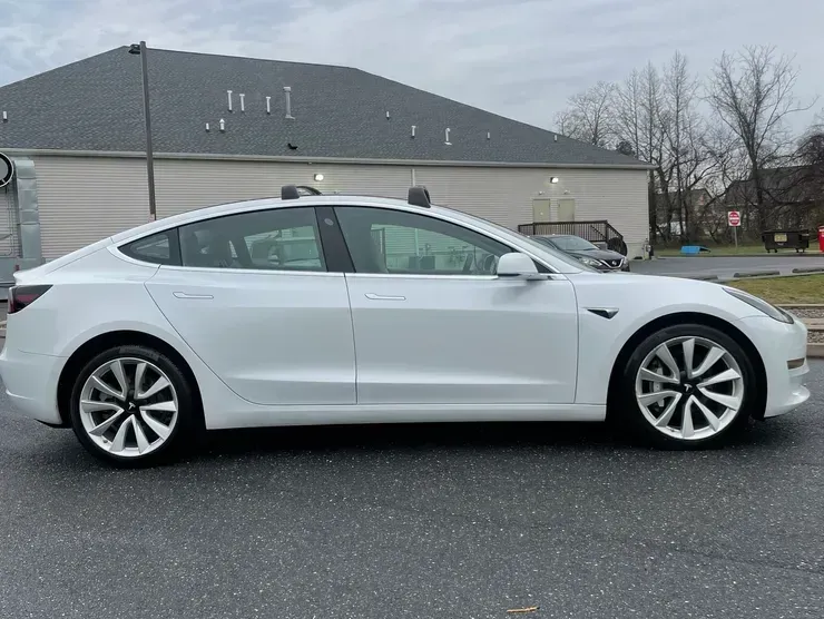 White Tesla sedan parked on wet pavement in front of a house on an overcast day