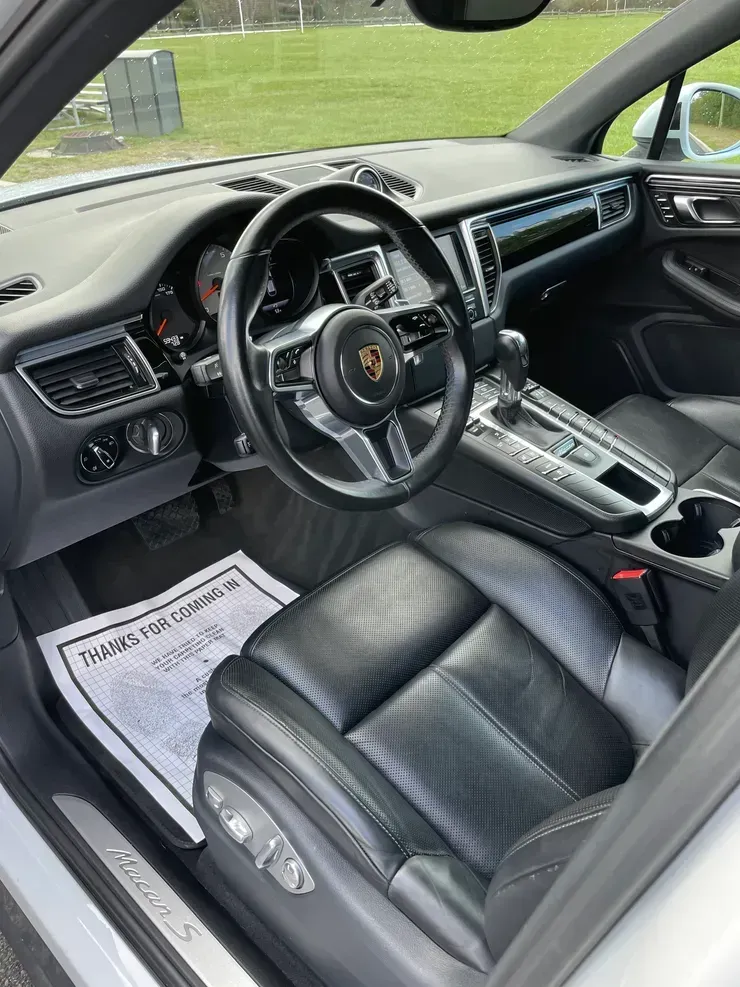 Black Porsche interior with leather seats, steering wheel, and center console, viewed from the open driver’s door