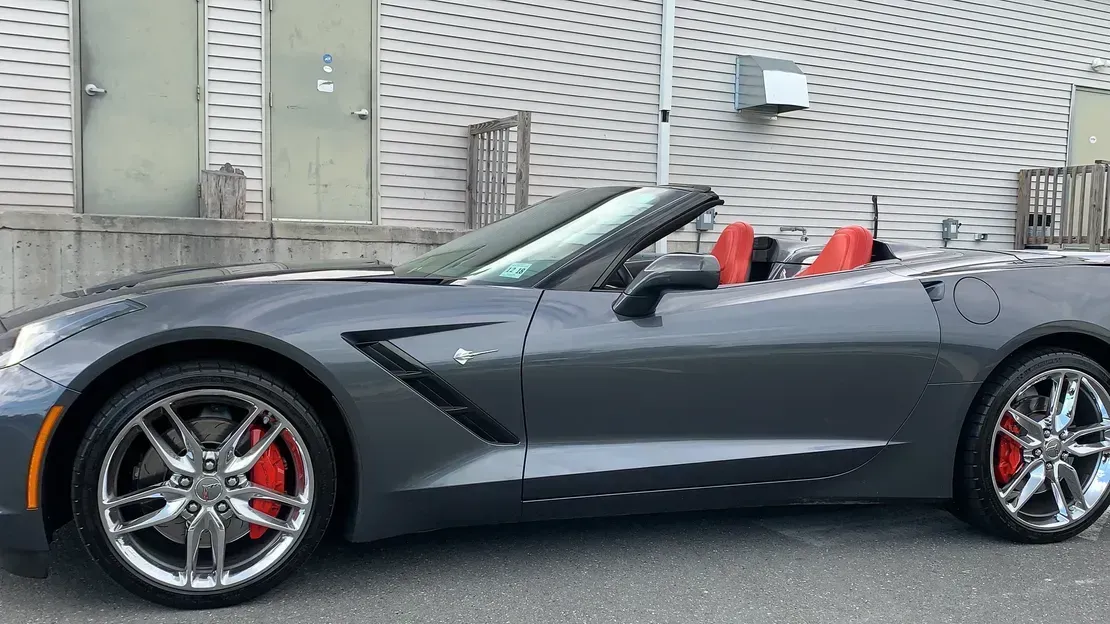 Dark gray convertible sports car with red seats parked beside a building.