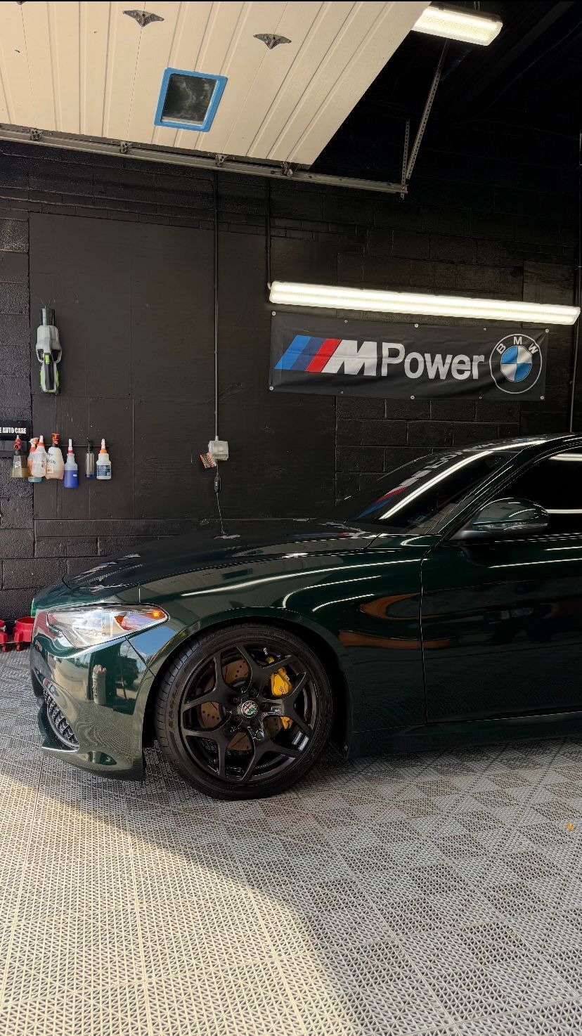 Dark green sports car in an indoor garage with an M Power sign on the wall.