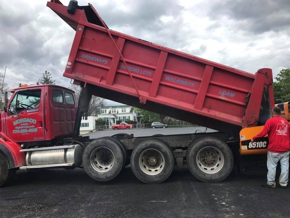 A man in a red shirt is standing next to a red dump truck