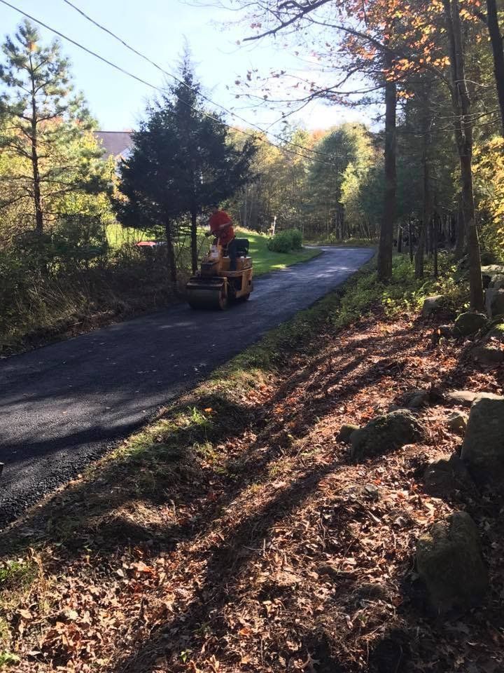 A man is driving a tractor down a road in the woods