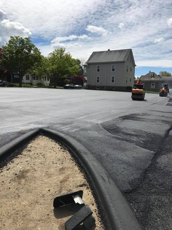 A lot of asphalt is being rolled in a parking lot.