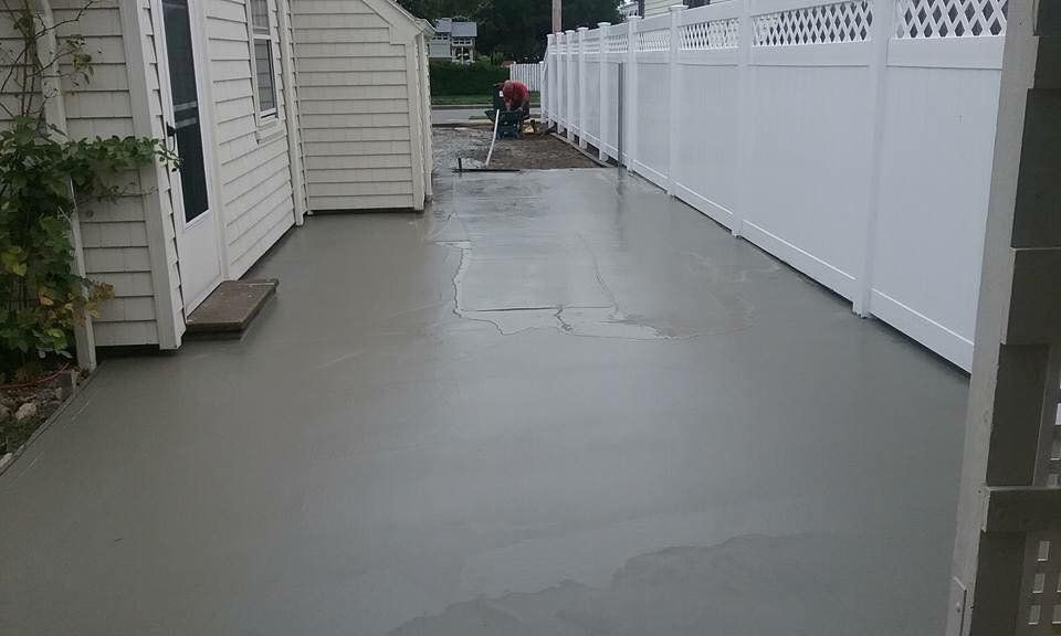 A concrete driveway with a white fence and a white house in the background.